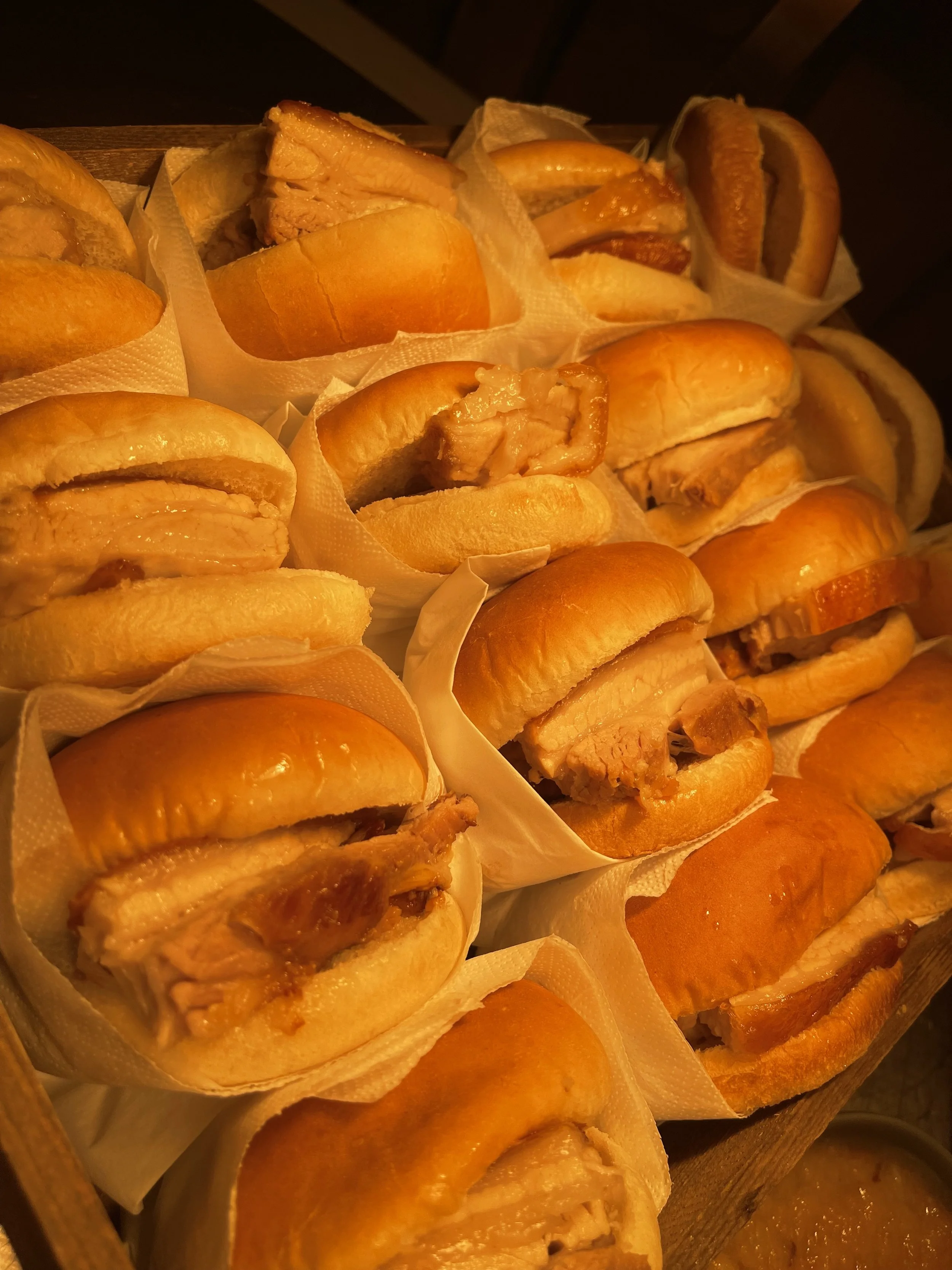 Close-up of baked bread rolls filled with meat, arranged in a basket lined with yellow paper.