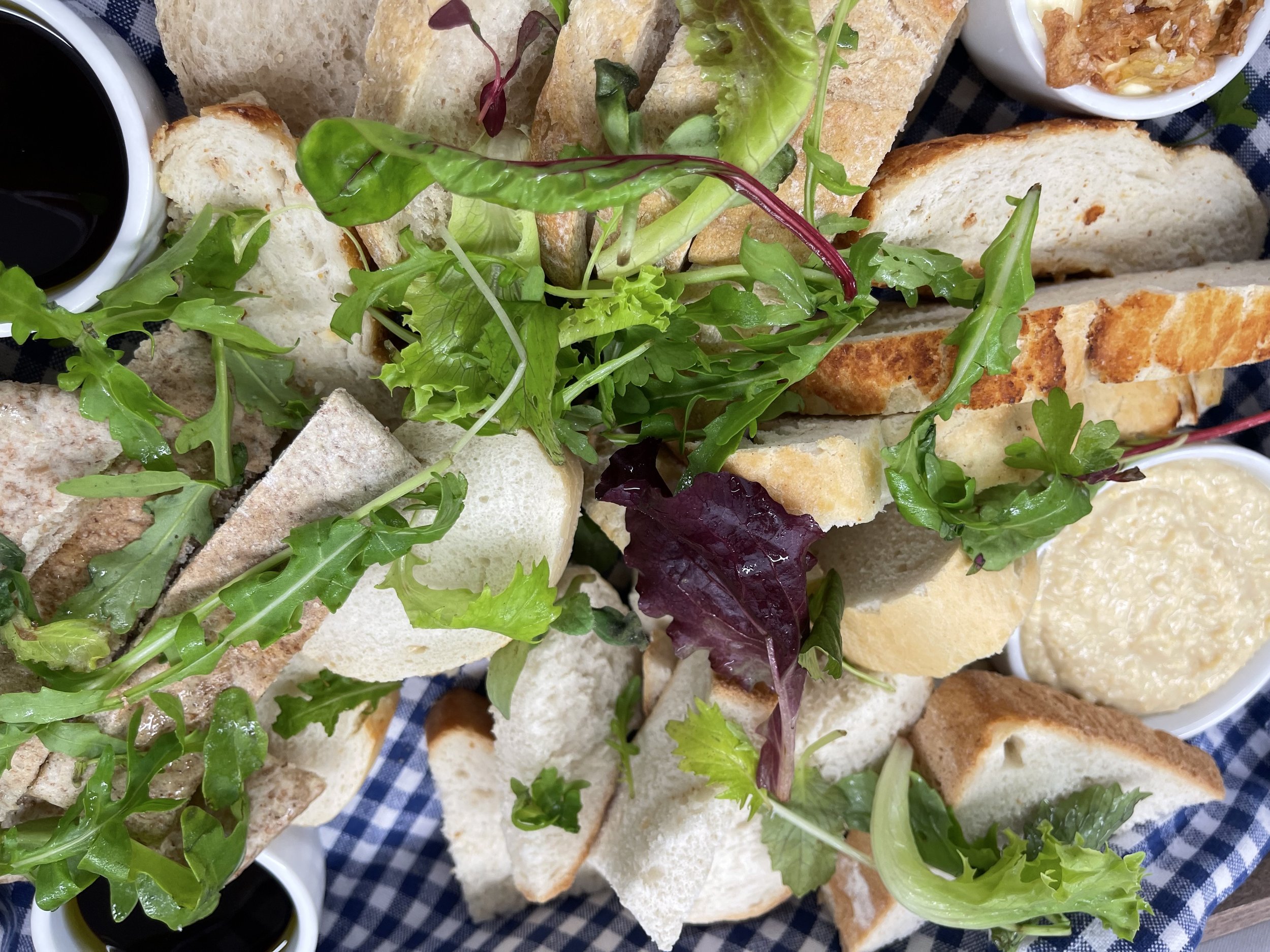 Assorted sliced bread and fresh mixed greens with small bowls of sauces or dips, on a checkered cloth.