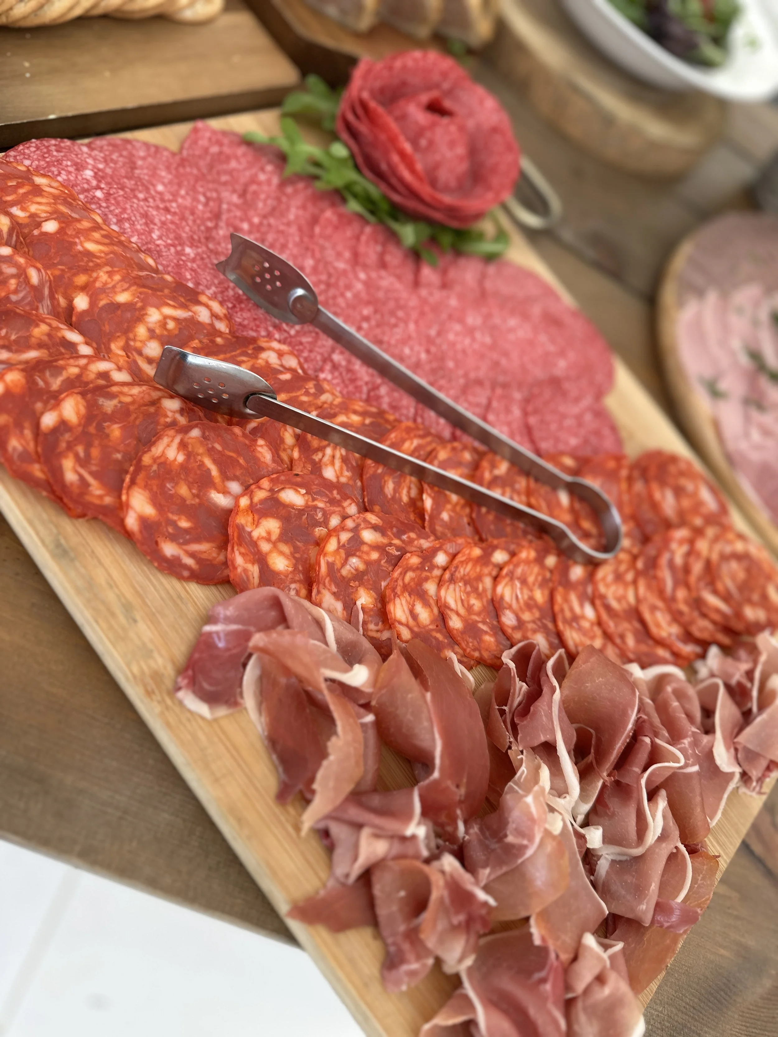 Assorted sliced cured meats, including salami, prosciutto, and other cold cuts, on a wooden serving board.