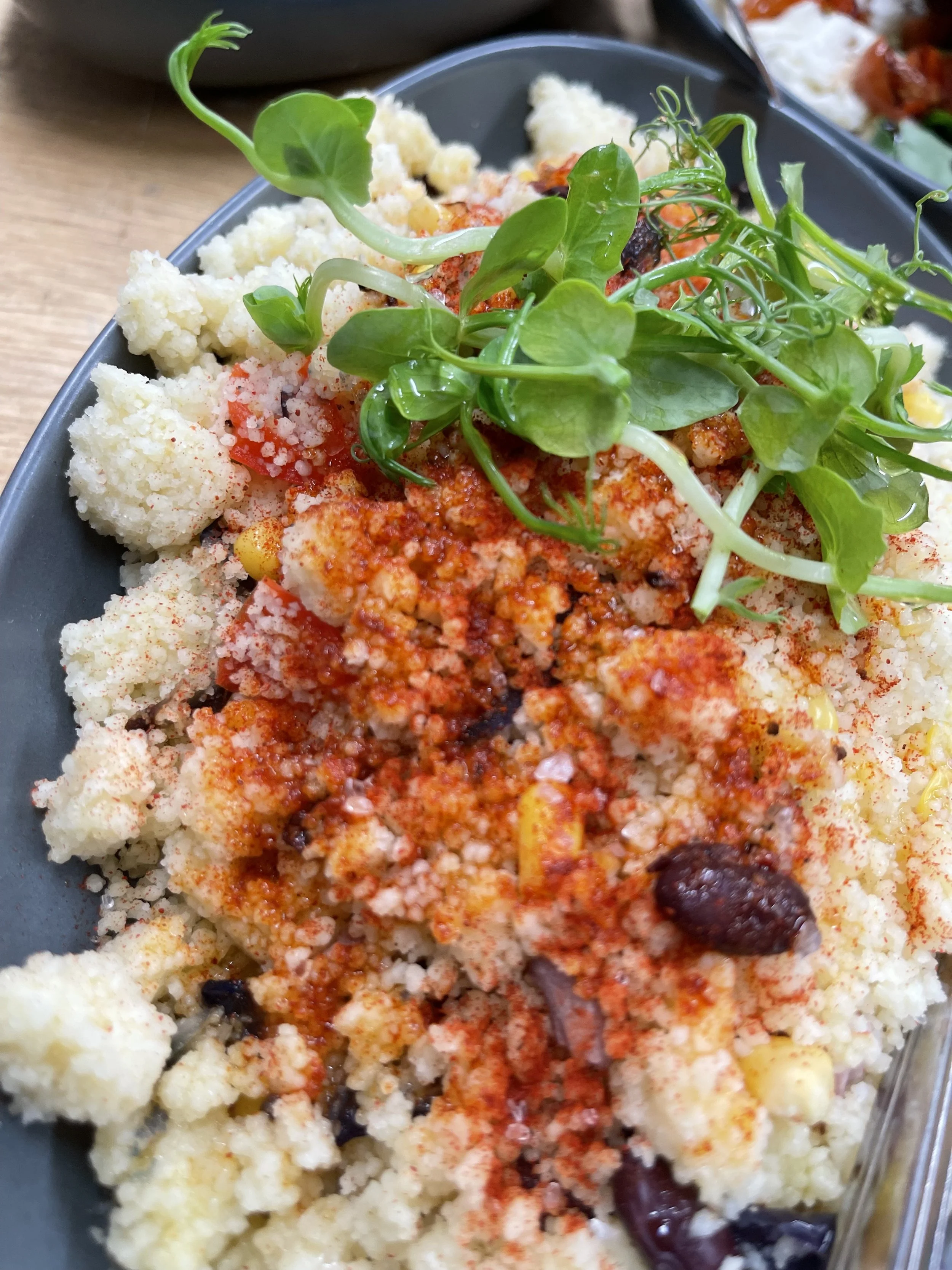 Close-up of a cauliflower salad with seasoning, garnished with fresh microgreens on top, on a black plate.