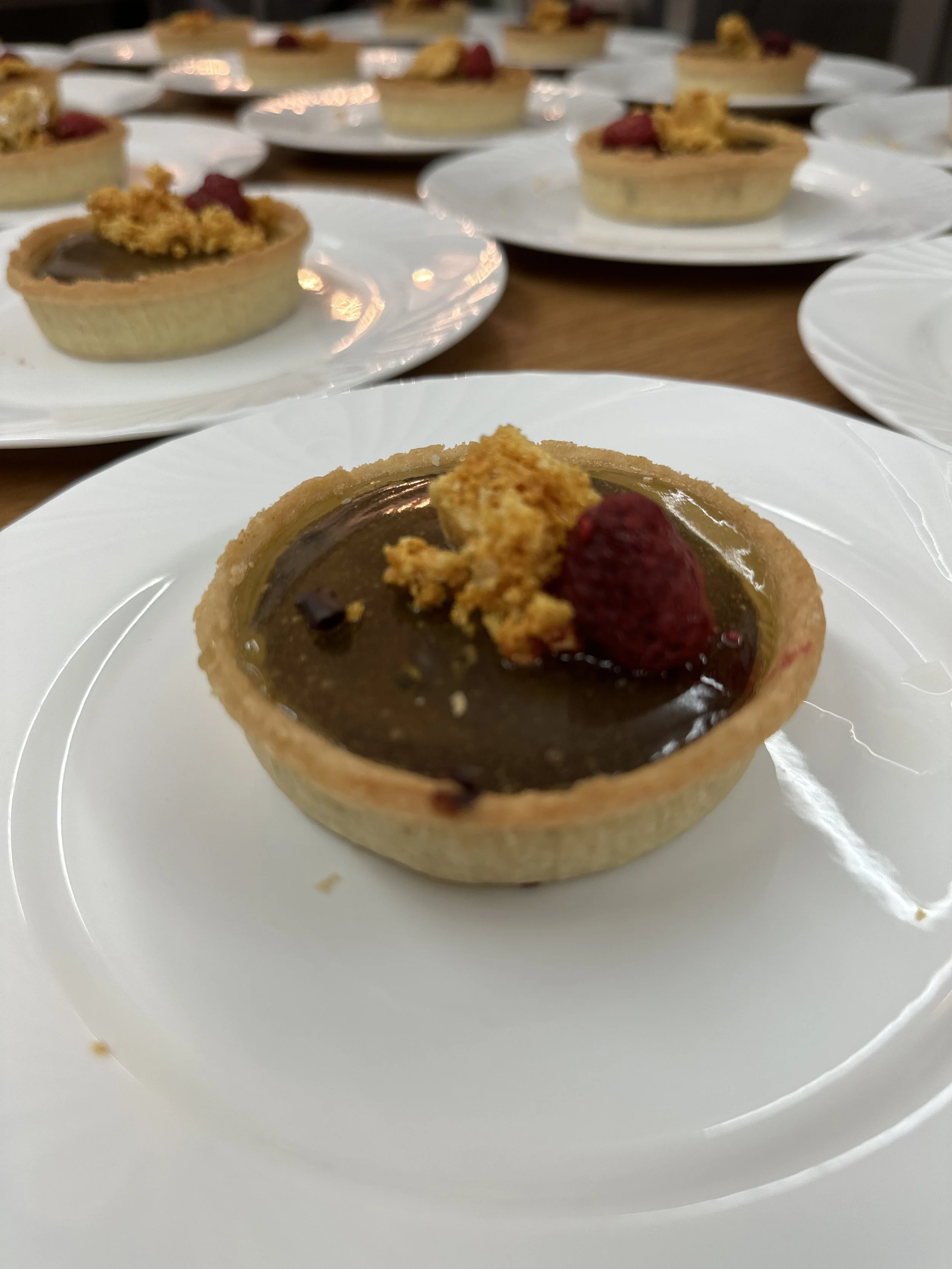 Chocolate tart garnished with a fresh raspberry and crumbled cookie on a white plate.