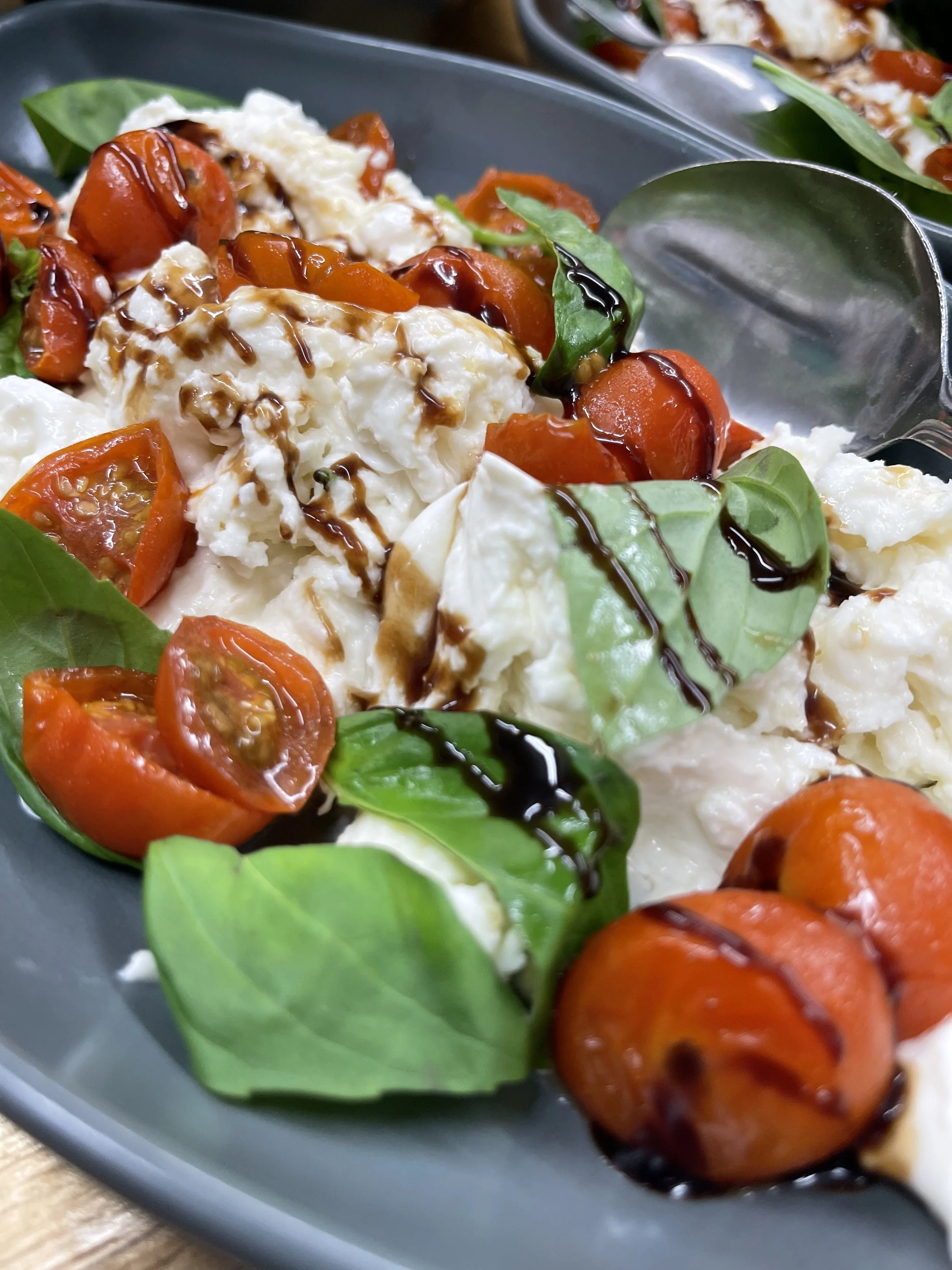 Caprese salad with cherry tomatoes, fresh basil, mozzarella, balsamic glaze, and olive oil on a dark plate.
