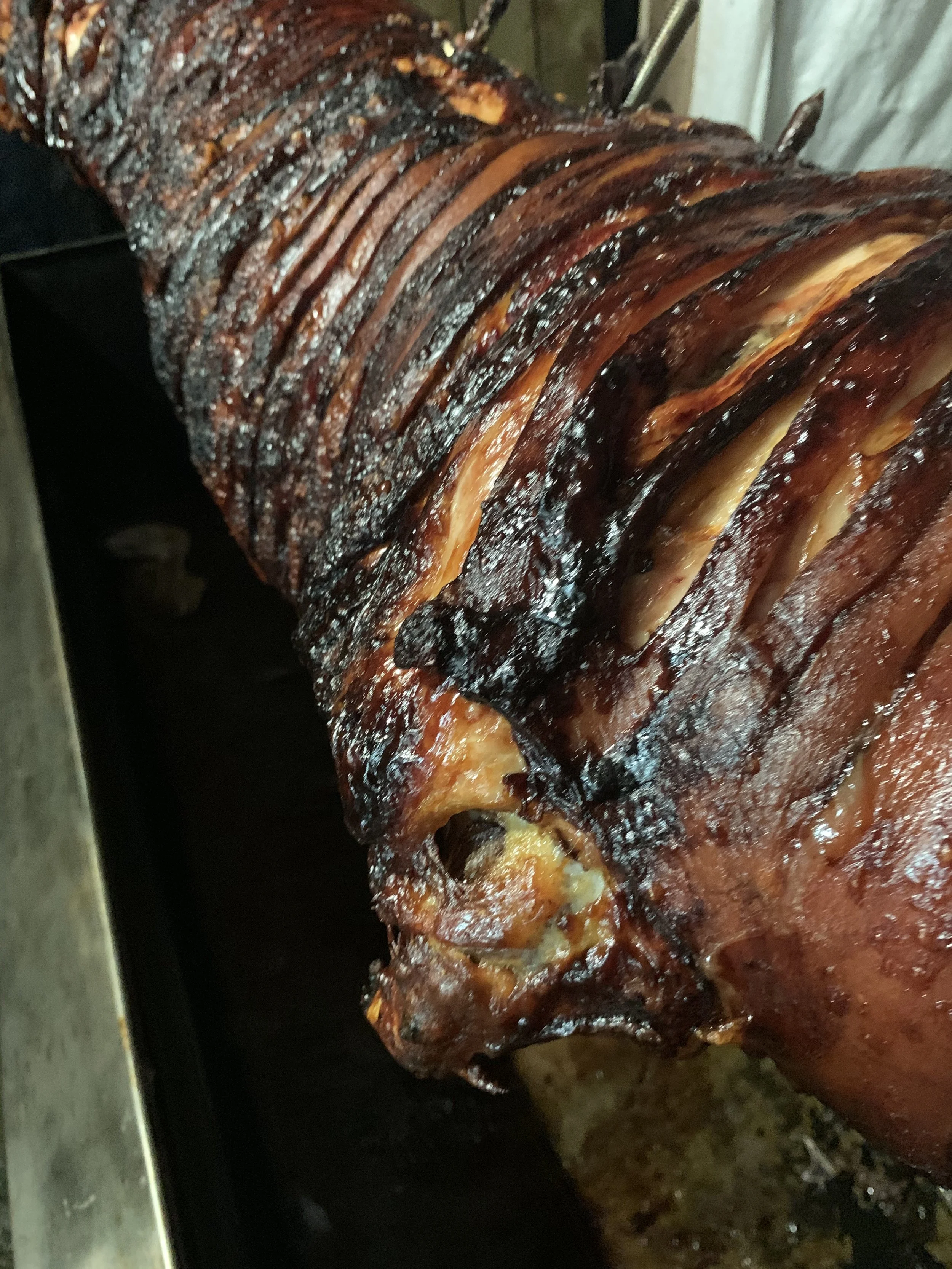 Close-up of a roasted pig with crispy, caramelized skin and sliced sections, resting on a tray.