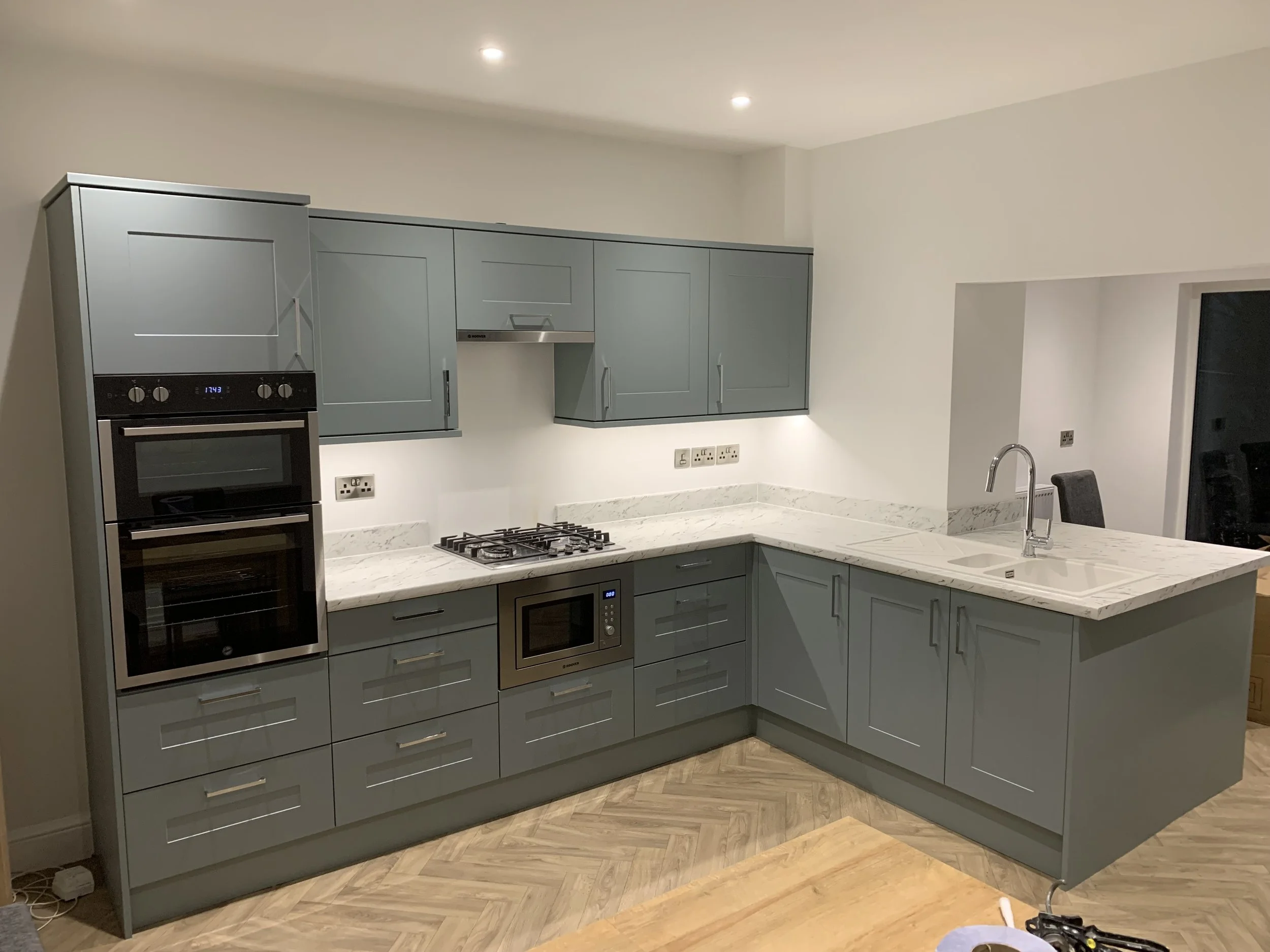 Modern kitchen with blue cabinets, white marble countertops, built-in oven, microwave, gas stovetop, and a sink with a faucet.