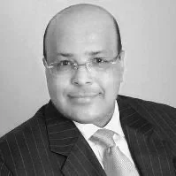 Portrait of a bald man wearing glasses, a pinstripe suit, white shirt, and a light-colored tie. The image is in black and white.