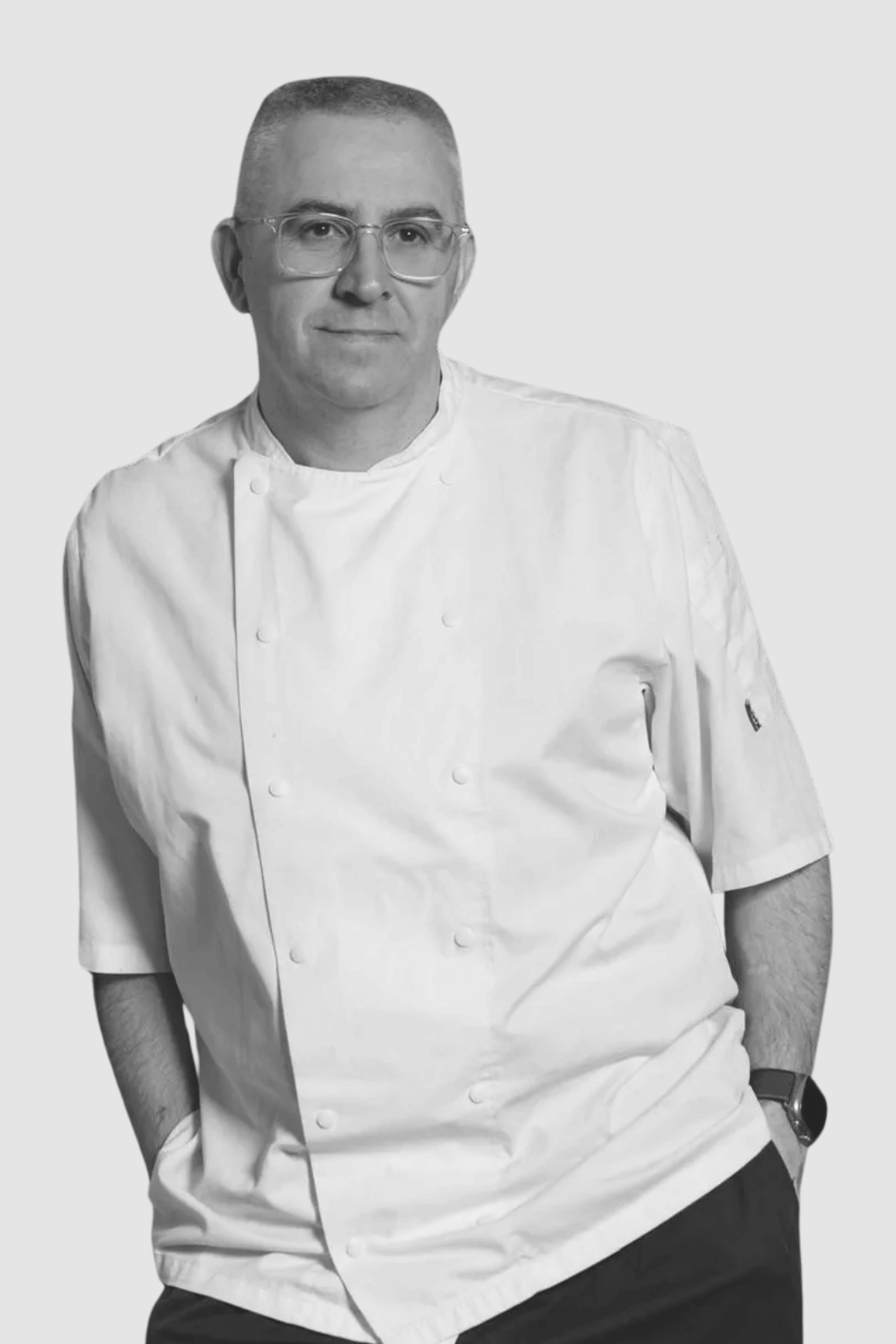 Chef wearing white uniform and glasses, in black and white.