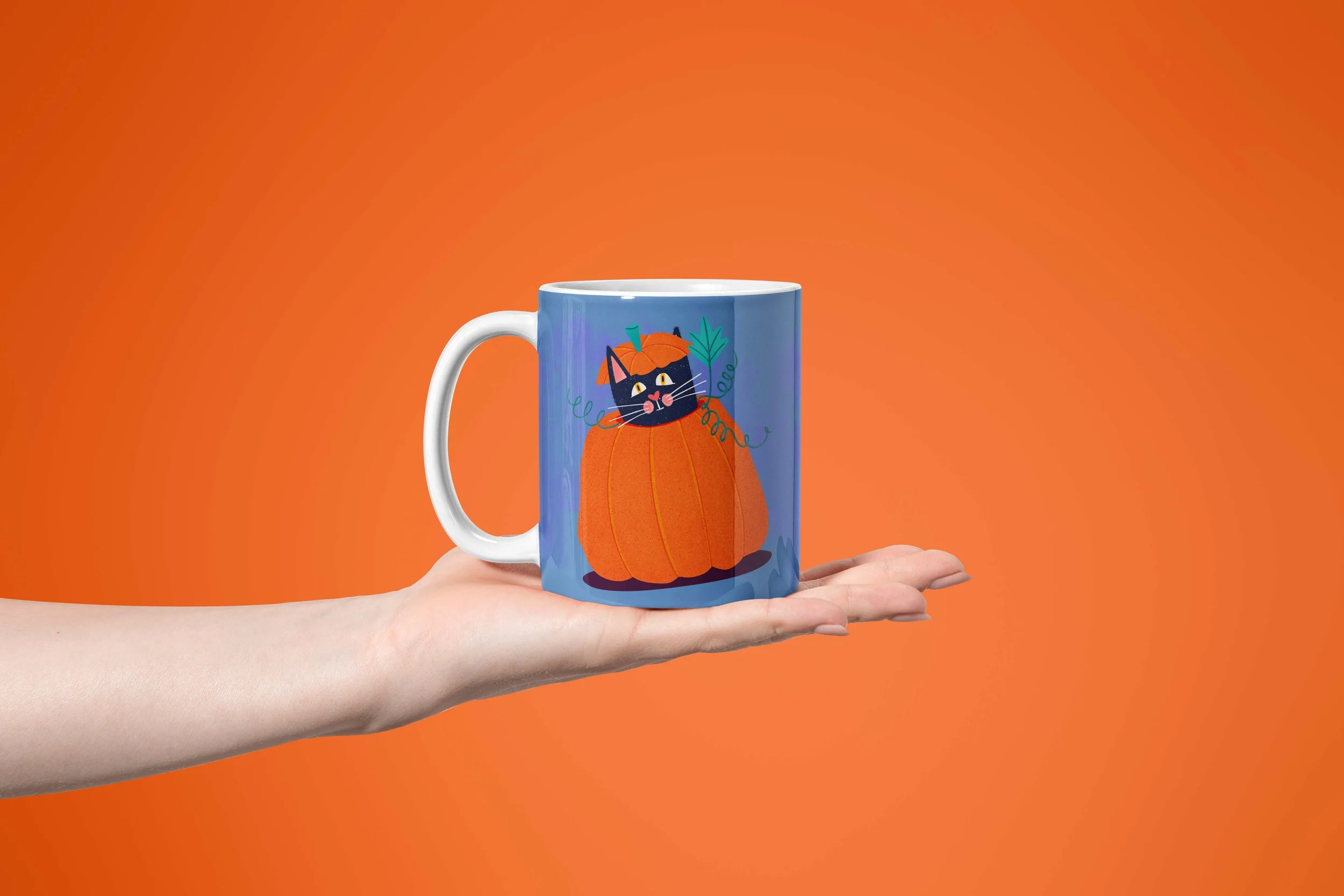 A hand holding a blue Halloween mug of a cat inside a pumpkin, over an intense orange background