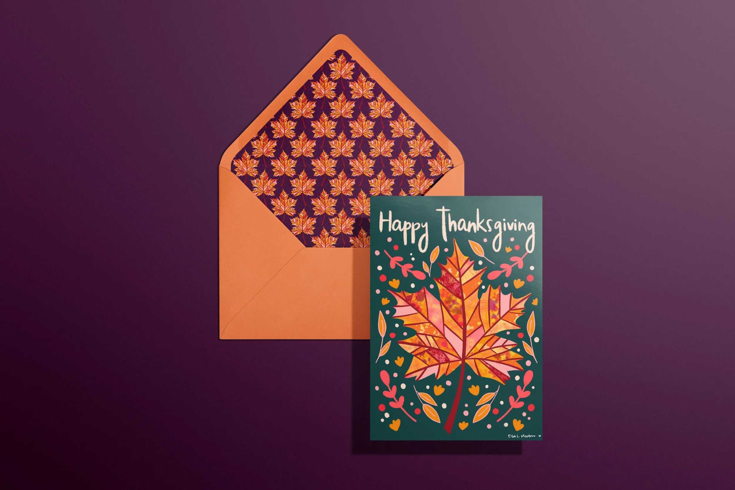 A card and envelope featuring leaves, branches and flowers in autumnal colors and the hand lettered message "Happy Thanksgiving". The envelope features a coordinating maple leaf pattern inside.