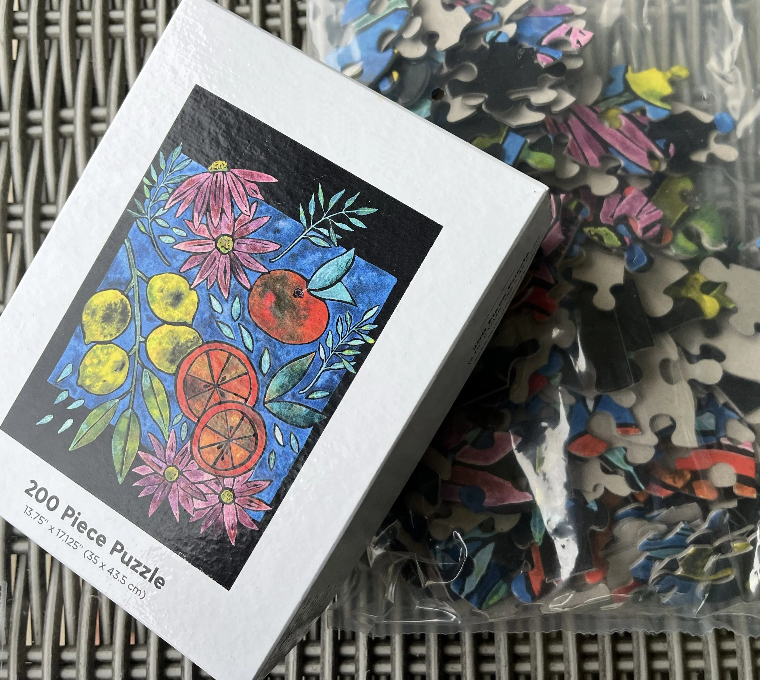 Image shows the box of a 200 piece puzzle with a citrus and flower illustration. The box sits atop the puzzle pieces.