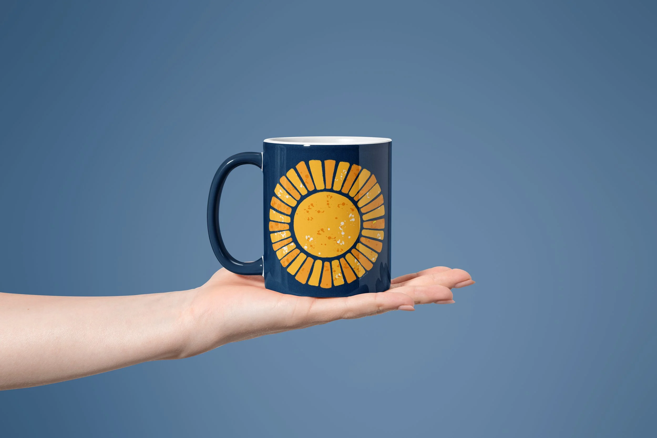 Hand holding a navy-colored mug with a yellow sun mosaic-style illustration 