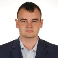 Portrait of a man in a suit with short dark hair against a plain background.