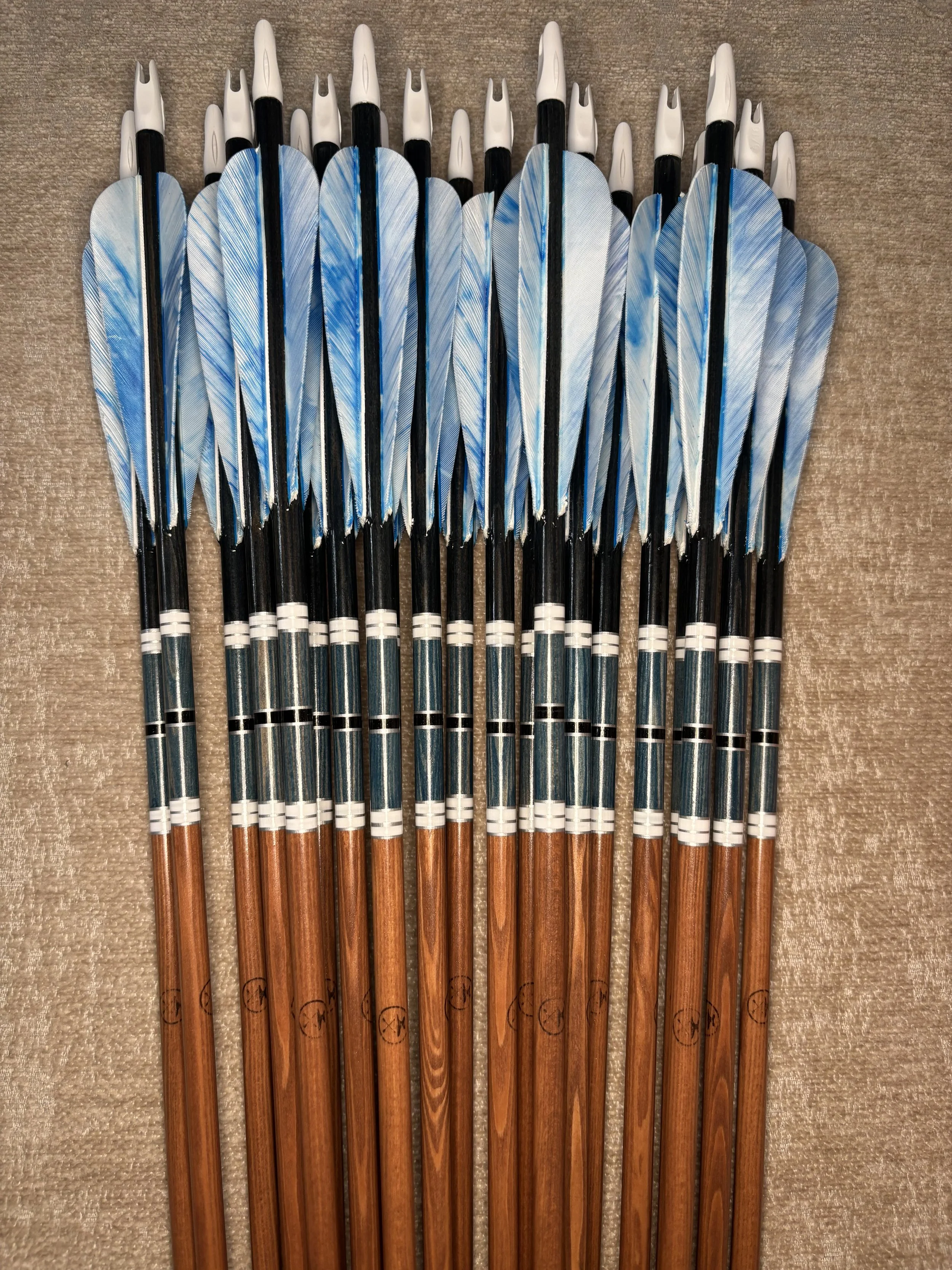 Set of hunting arrows with blue and white fletching, and wooden shafts, arranged in a row on a beige surface.