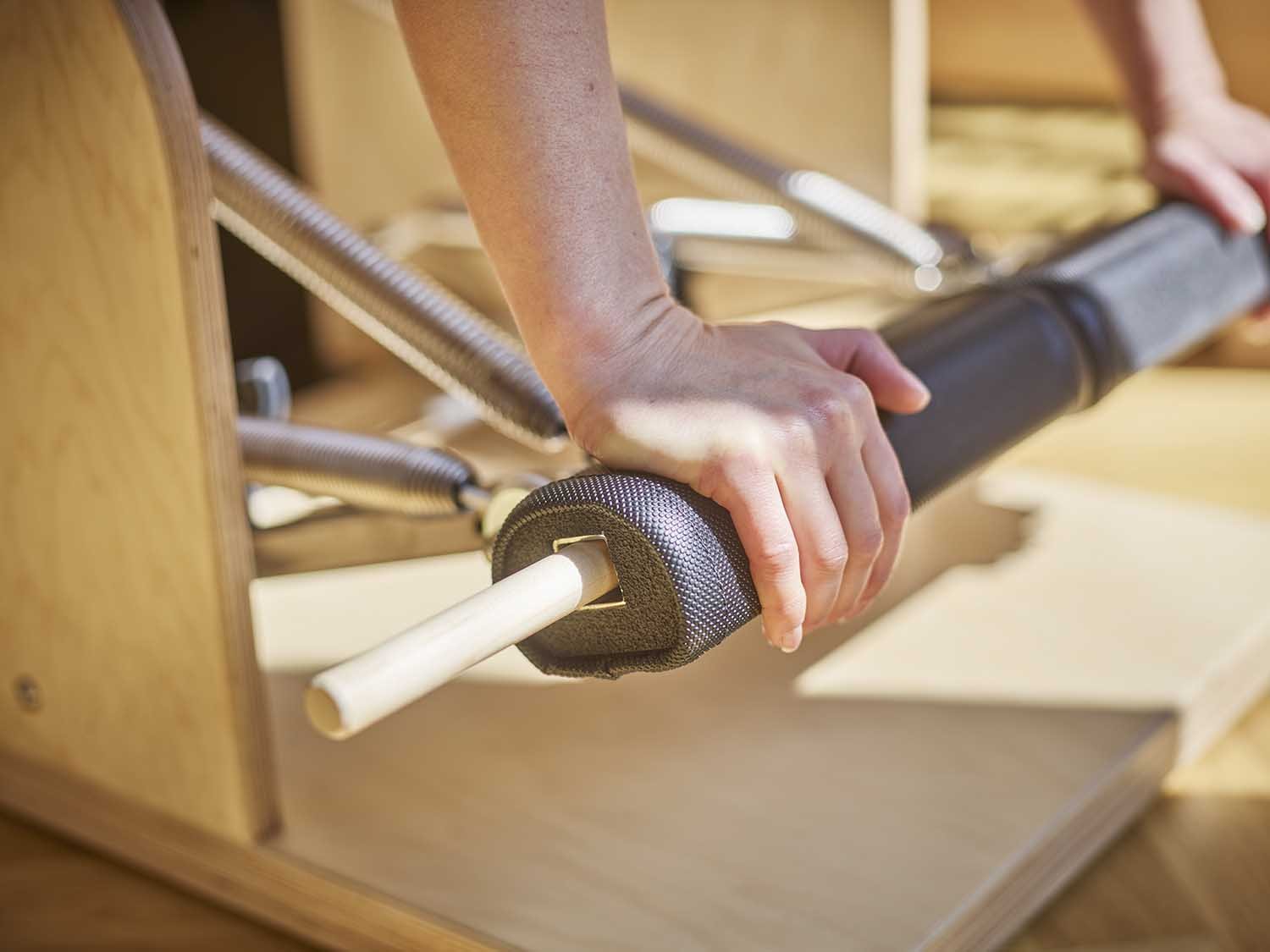 Person hält einen Griffteller auf einem Zugstab bei einer Pilates-Übung.
