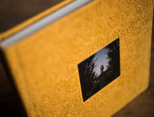 A framed photograph of a person standing outdoors on a hill with trees, against a sky, mounted on a textured yellow wall.