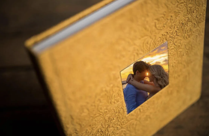A yellow photo album with an embossed cover, opened to a page showing a couple kissing at sunset.