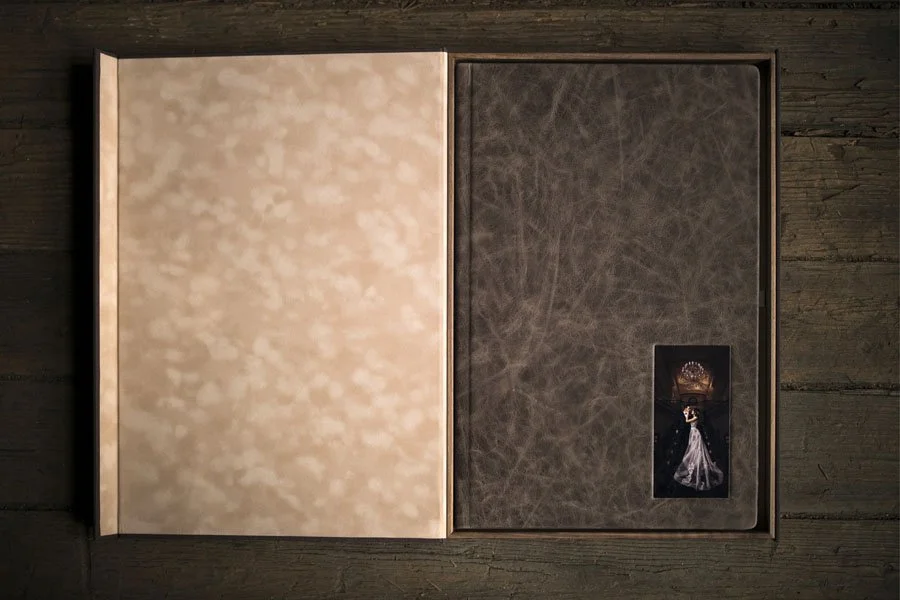 Open photo album on a wooden surface, with the left page blank and the right page displaying a small photo of a woman in a white dress, standing in front of a crown-like decoration.