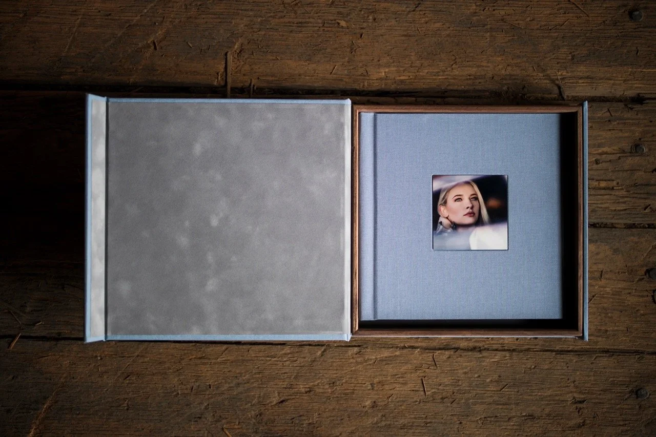 An open photo album resting on a wooden surface showing a portrait of a woman with blonde hair and makeup.