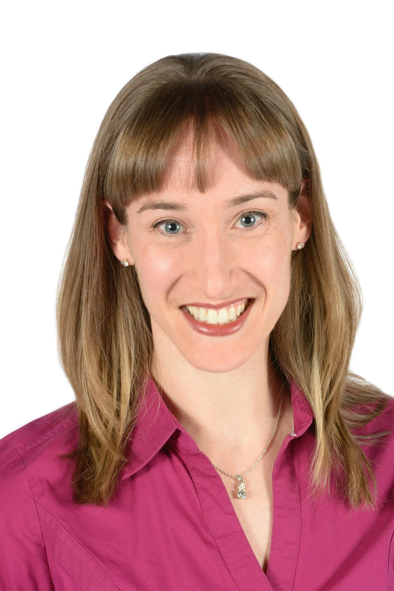 A light-skinned person smiling at the camera with light brown, medium length hair, wearing a pink collared shirt.