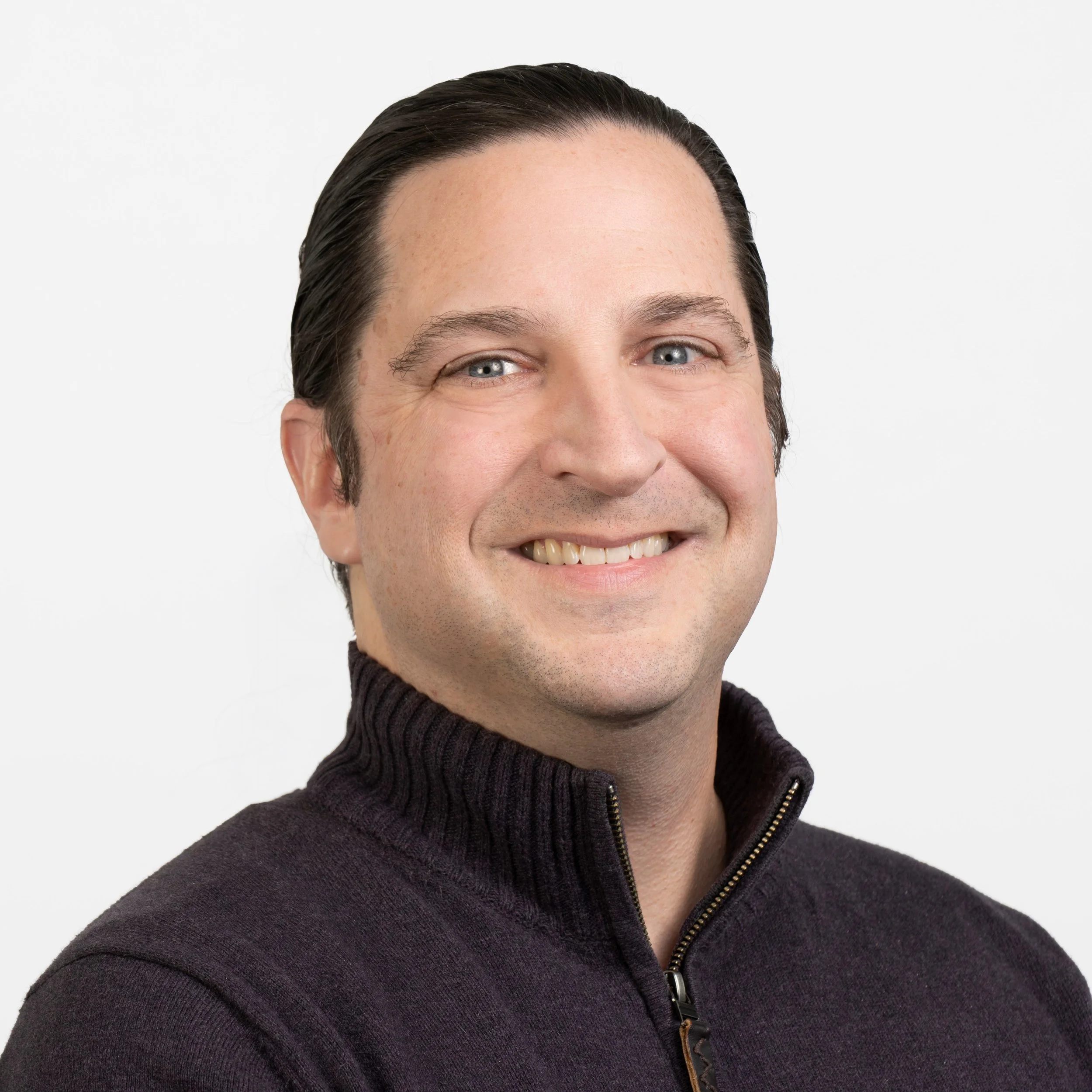 Man with dark hair wearing a dark sweater, smiling.