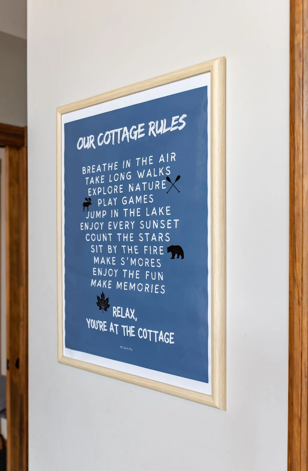 Blue sign with white text titled 'Our Cottage Rules' listing outdoor and nature activities surrounded by small icons of a moose, bear, and leaf.