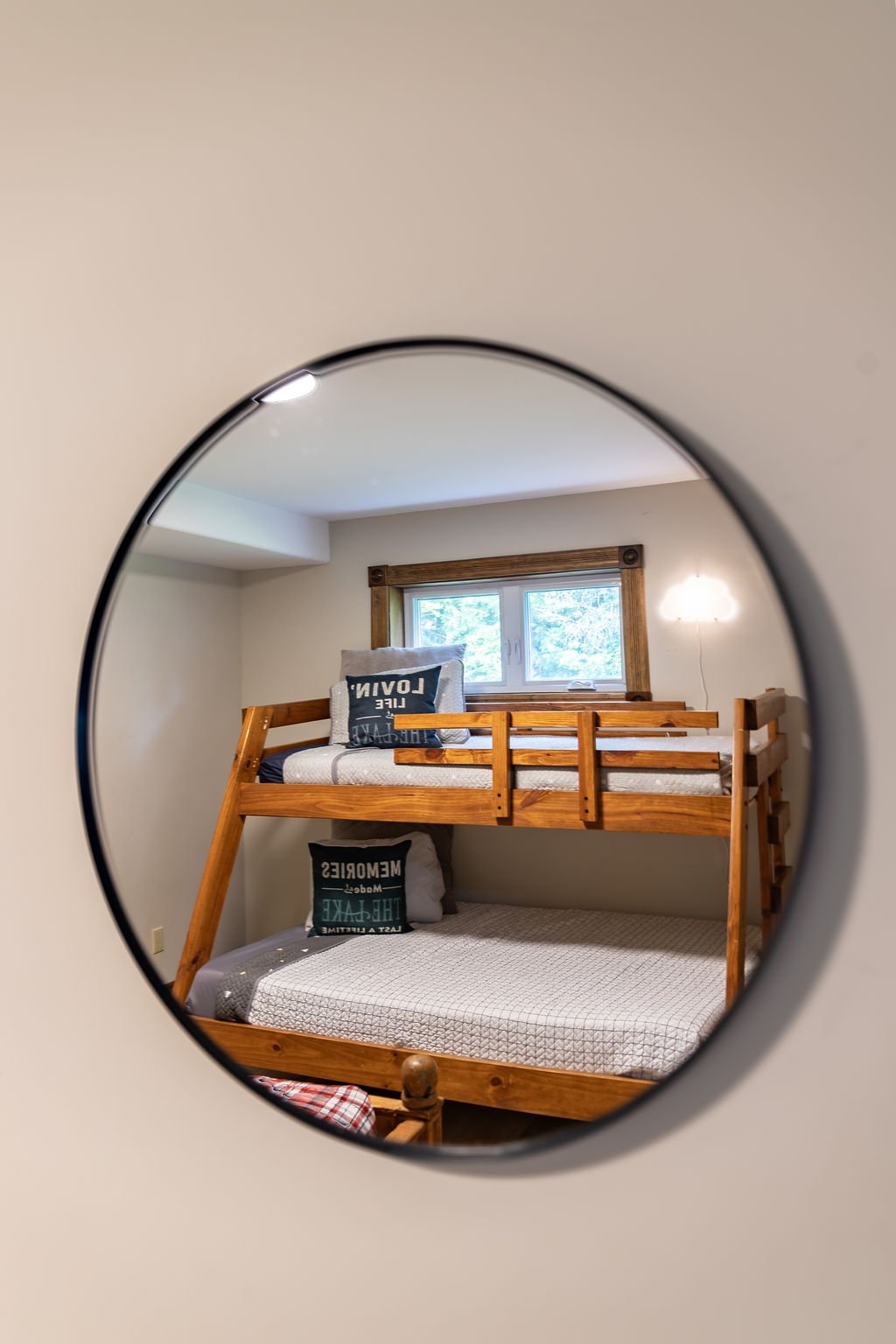 A mirror reflecting a room with a bunk bed, a window with wooden trim, and some decorative pillows.