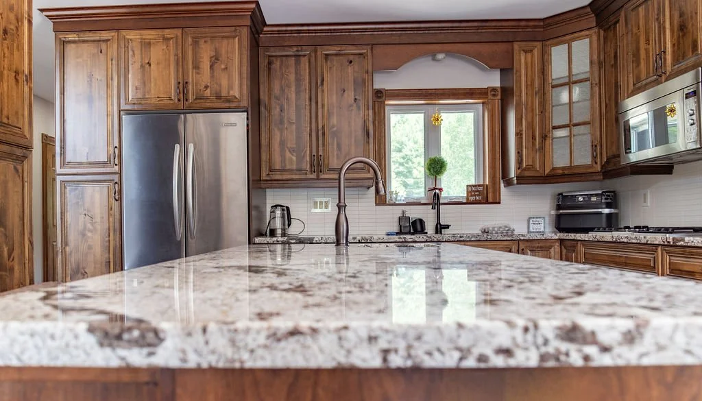 Kitchen with wooden cabinets, granite countertops, stainless steel refrigerator, microwave, and a window with greenery outside.