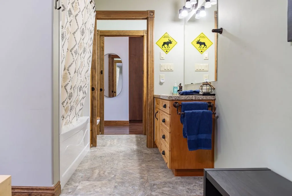 Bathroom with wooden vanity, blue towels, mirror, and wall-mounted lights, with a bathroom shower curtain visible on the left.