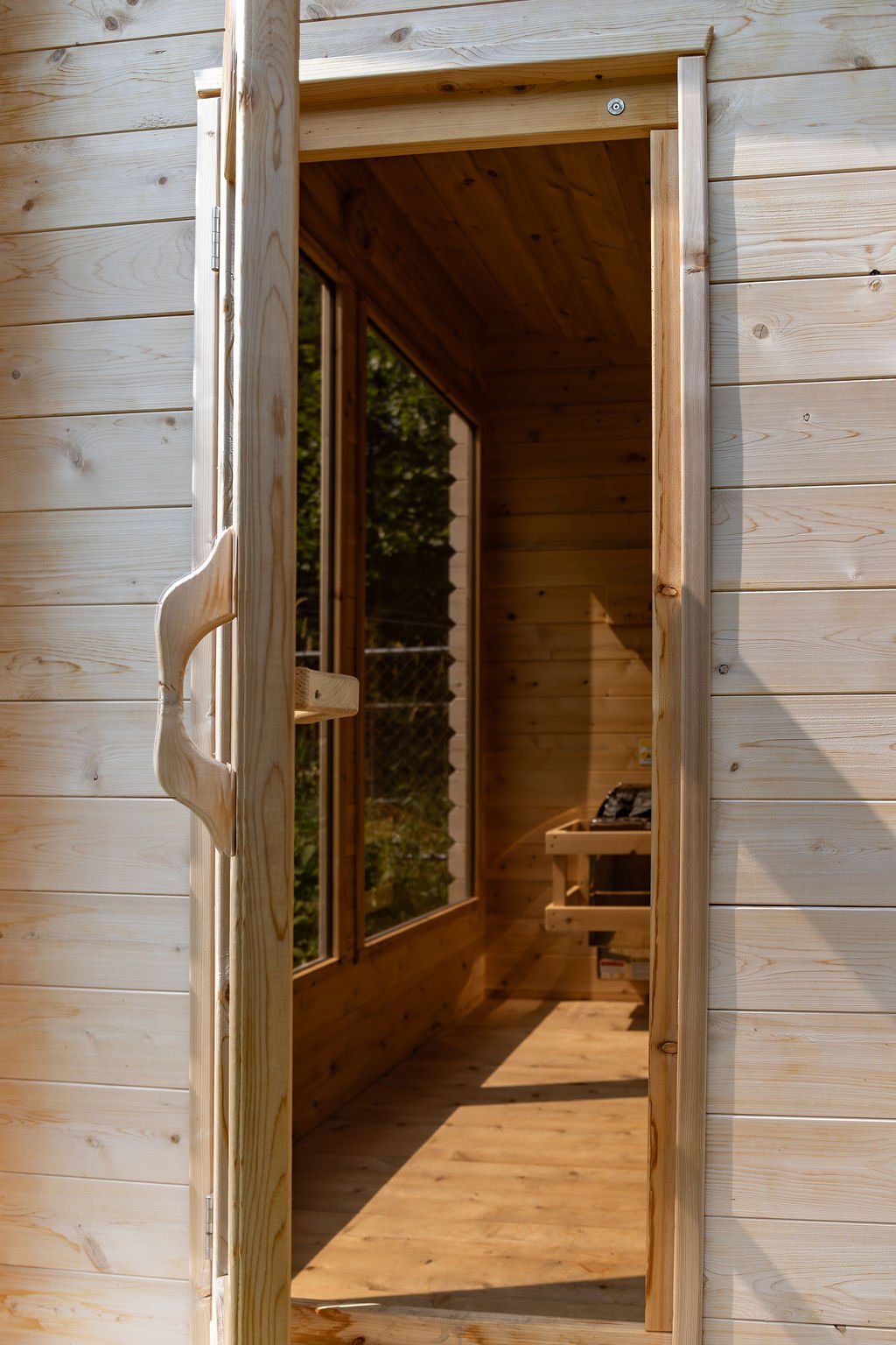 The image shows an open door to a wooden sunroom or porch, with wooden siding on the outside and a wooden interior, including a bench and a window.