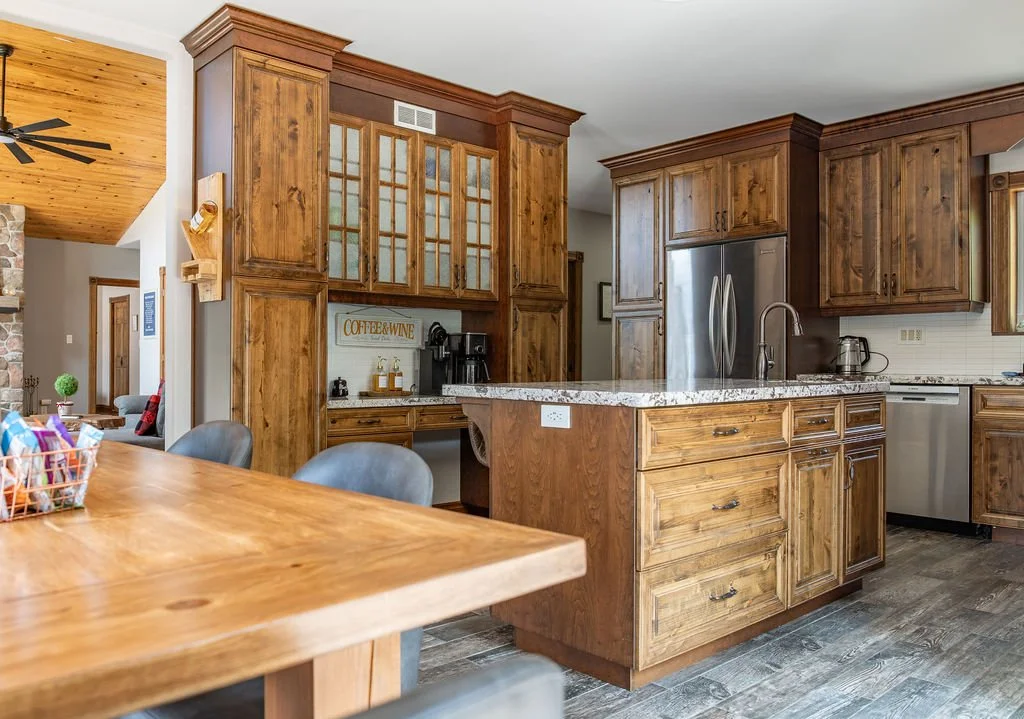Wooden kitchen with granite island, stainless steel appliances, and dining table with chairs.