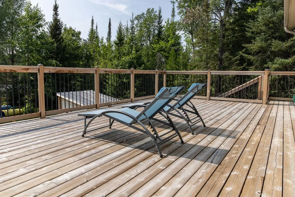 A wooden deck with three lounge chairs and a forested background.