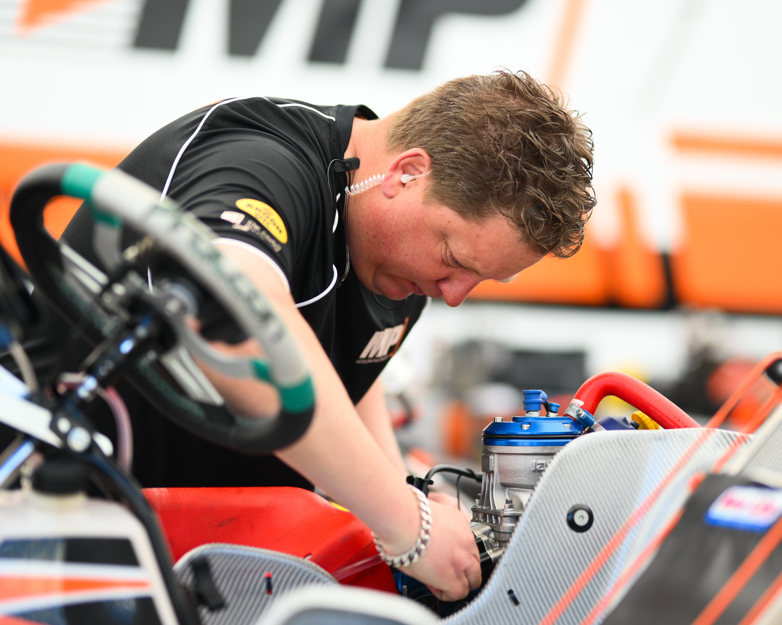 A man working on a race car engine in a garage, wearing a black shirt.