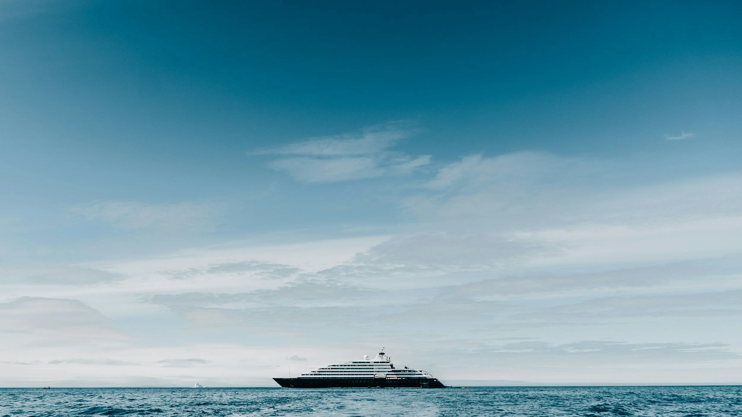 A luxury, modern cruise ship sailing on calm ocean waters under a partly cloudy sky. Blue Palm Travel knows the importance of luxury cruising. Jennifer Russell will help create the perfect, relaxing cruise for you.