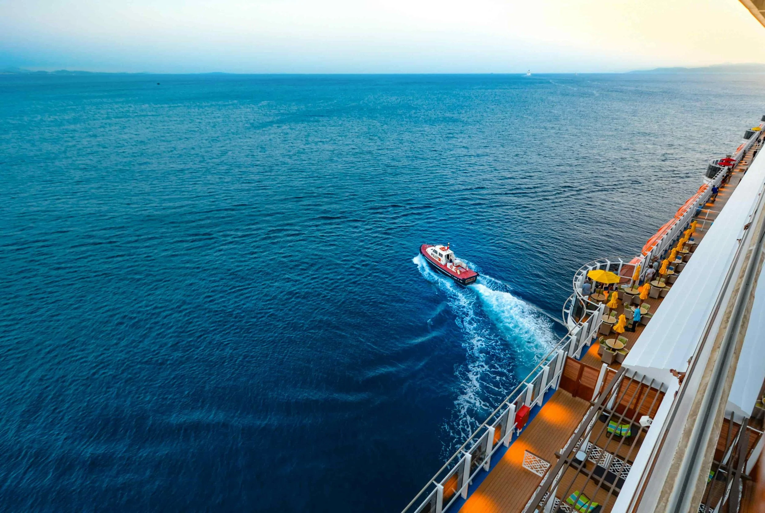 View of the ocean from a cruise ship deck with a small boat sailing nearby.