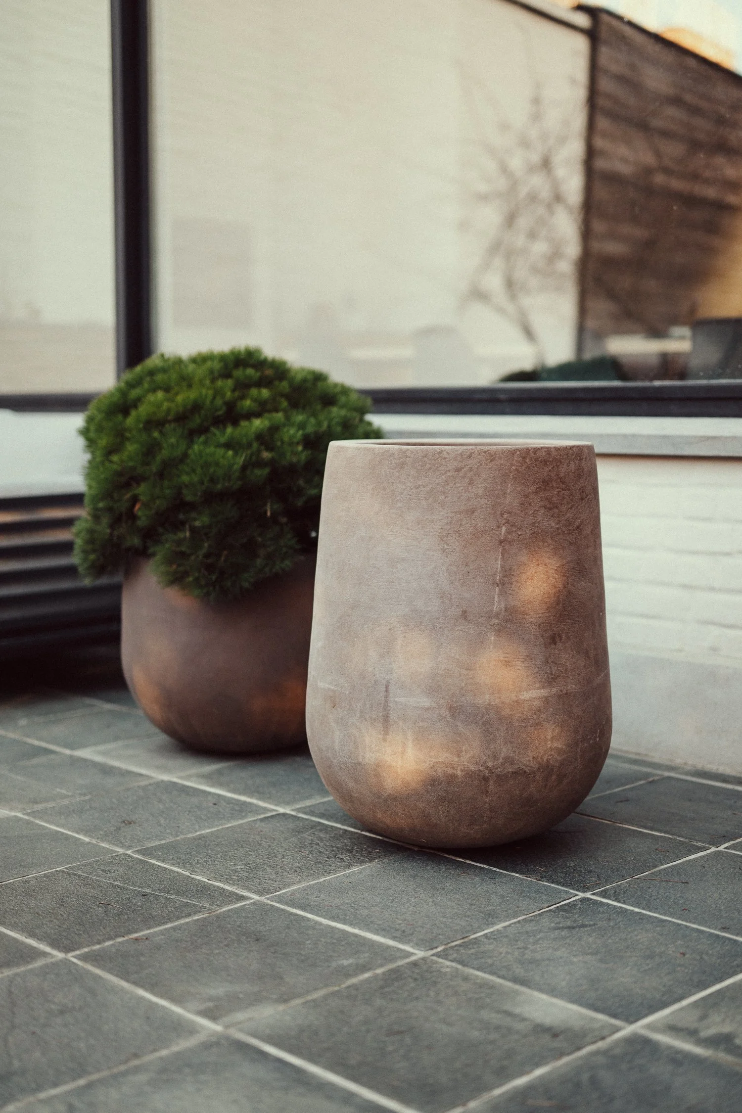Grote ronde lege bloempot in een tuin met veel paarse bloemen en groene planten.