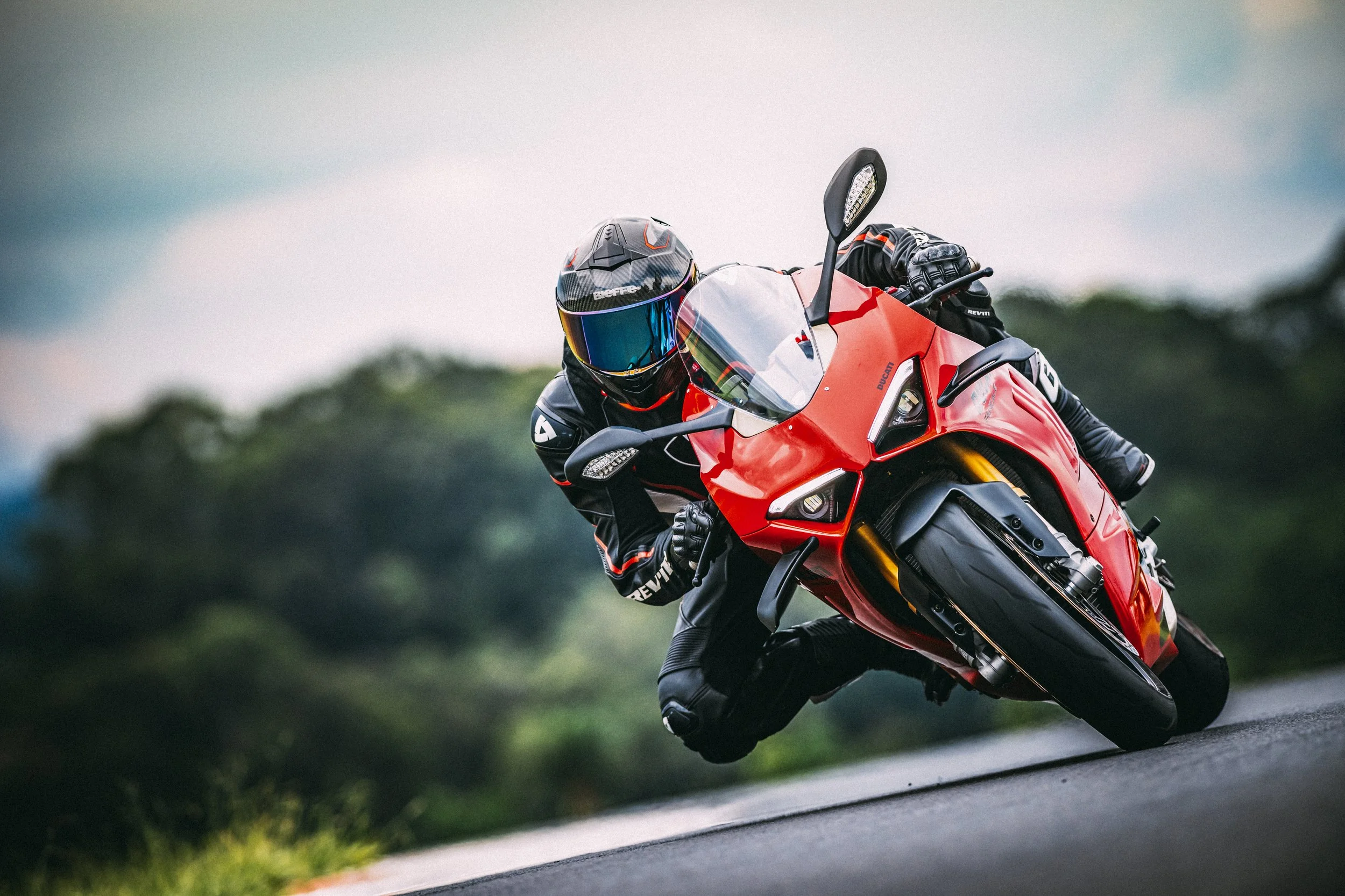 Motorcycle rider leaning into a turn on a red Ducati Panigale V4S on a curved road with greenery in the background.