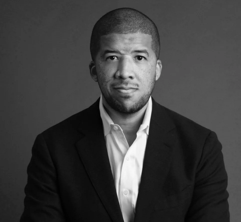 Tyler Scriven in a suit and white shirt against a plain background, black and white.