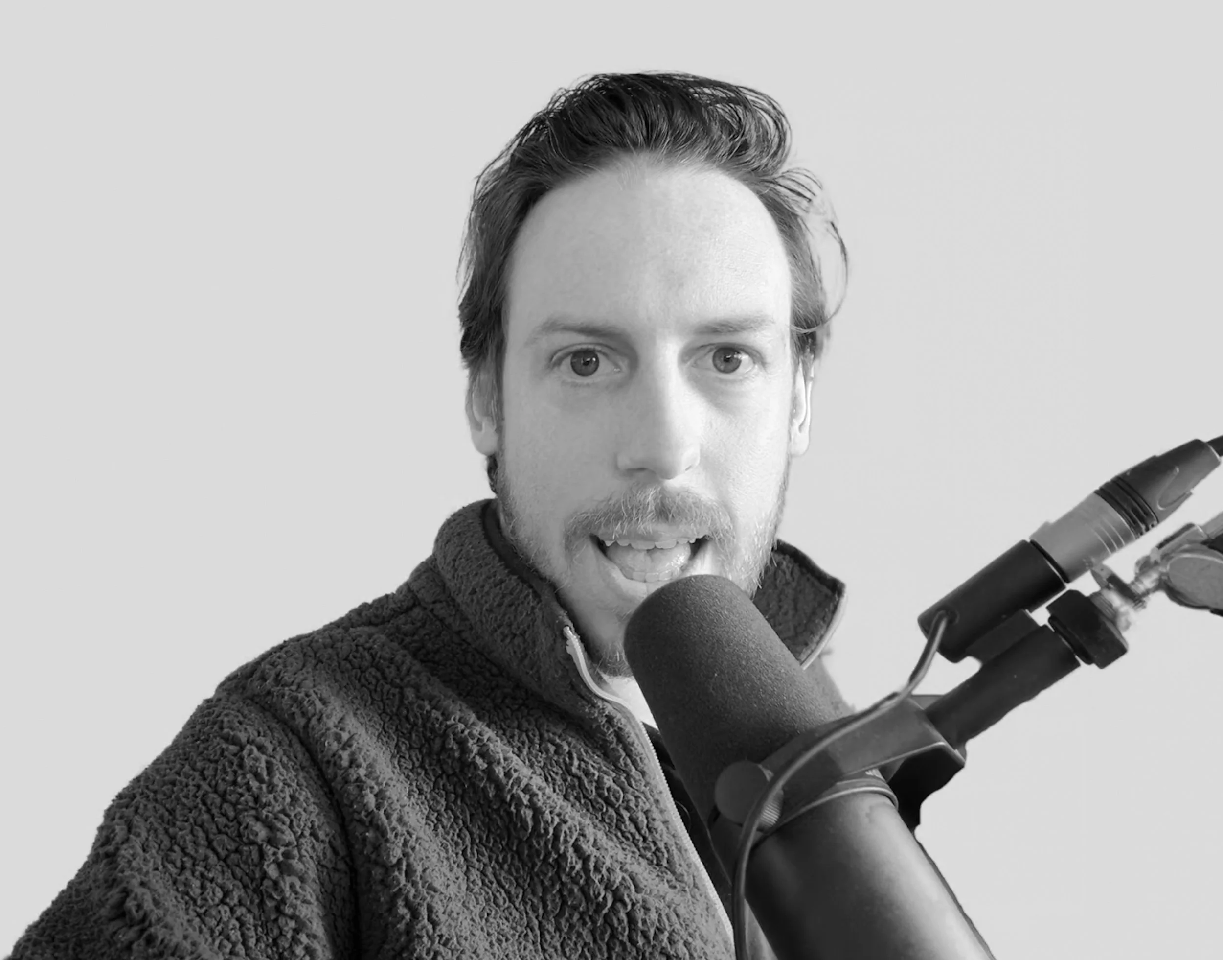 Tim Cakir speaking into a microphone, wearing a fleece jacket, black and white image.