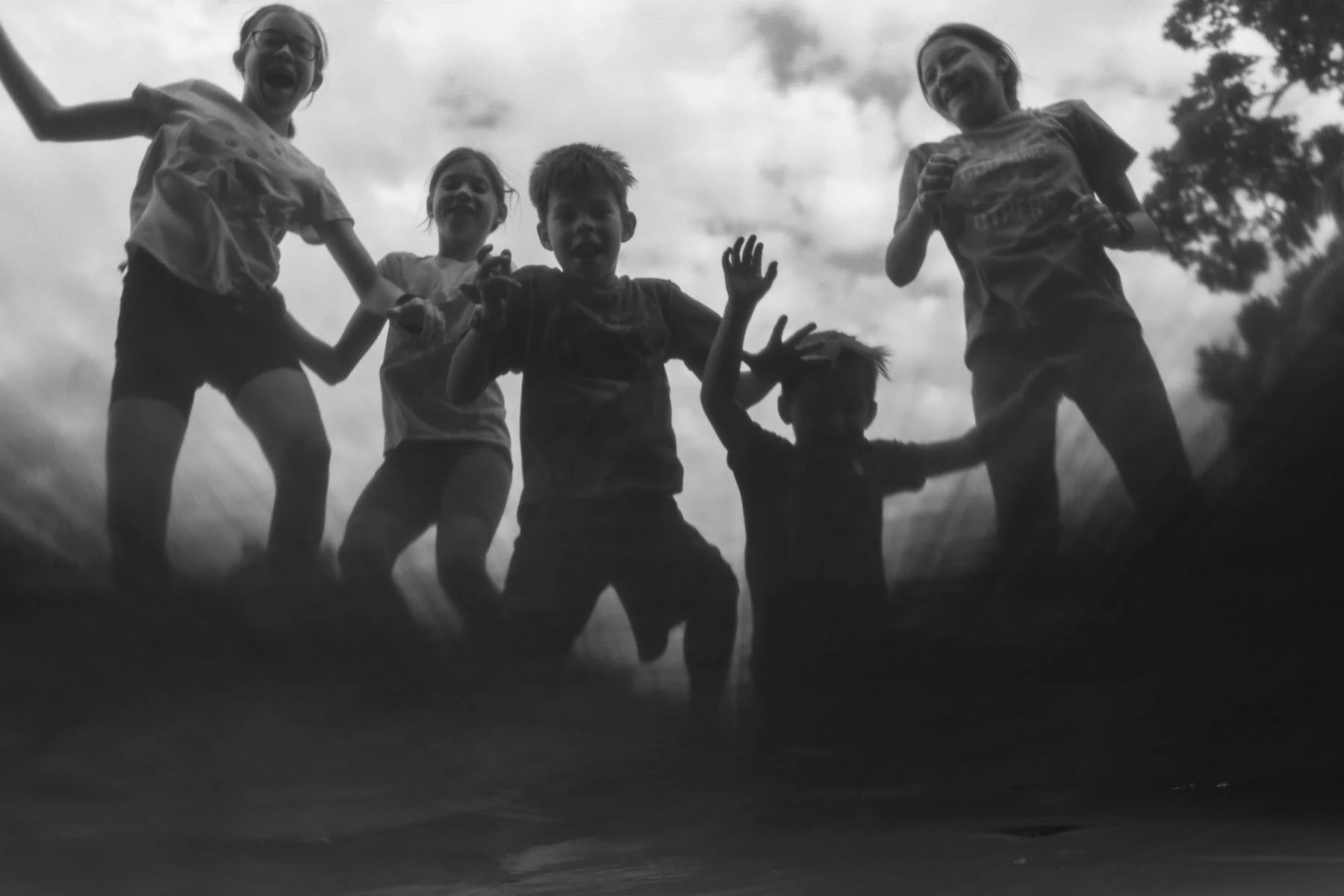 Silhouettes of five children playing and laughing outdoors against a cloudy sky, viewed from a low angle.