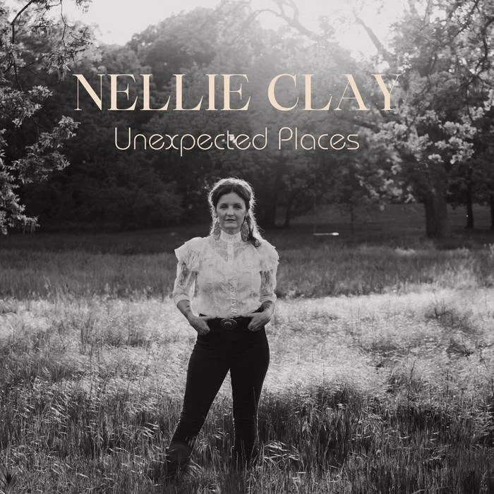 Black and white cover photo of Nellie Clay's album titled "Unexpected Places" with a woman standing in a grassy field with trees in the background.