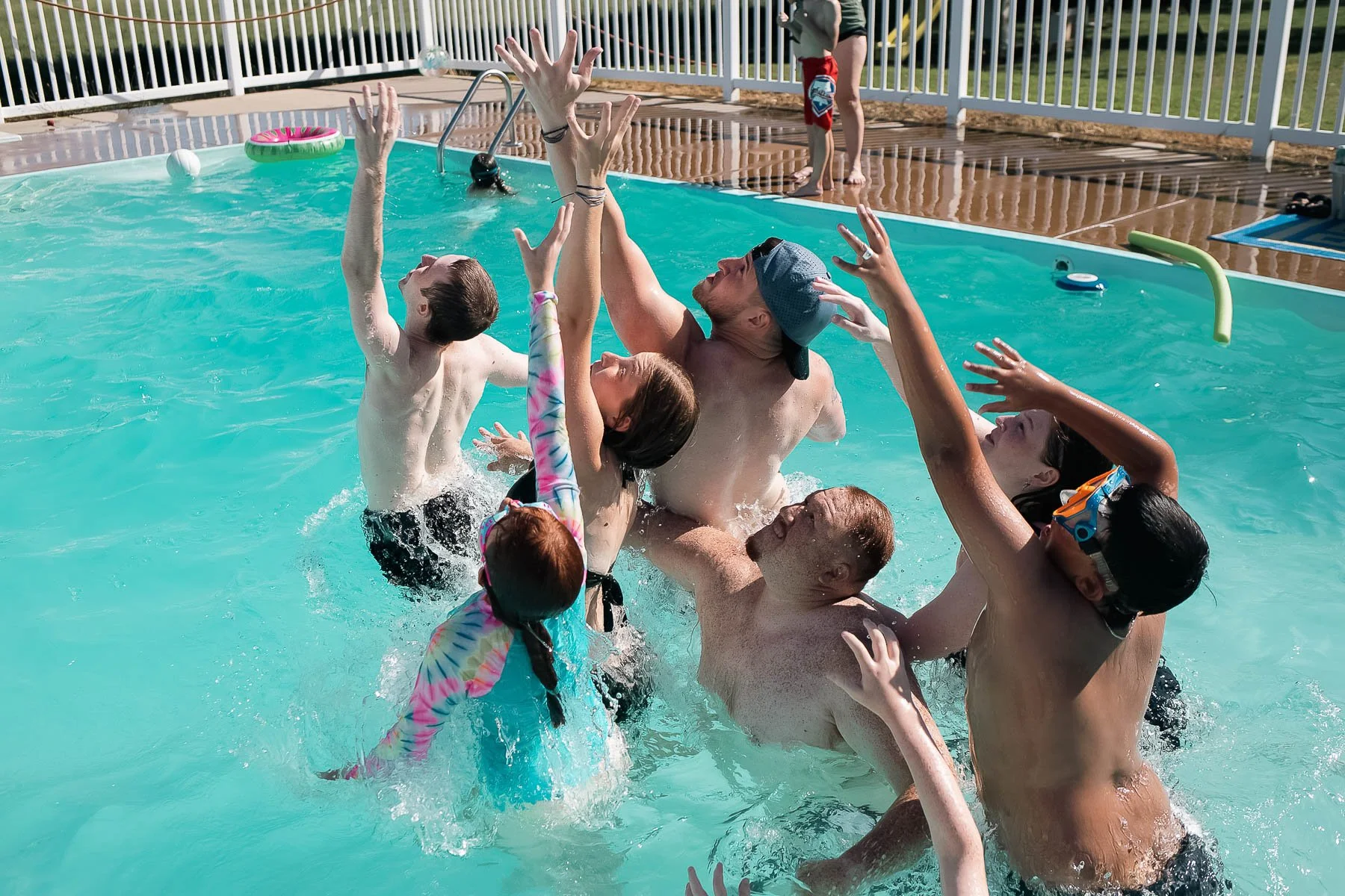 Group of people, including children and adults, playing and splashing in a swimming pool during daytime