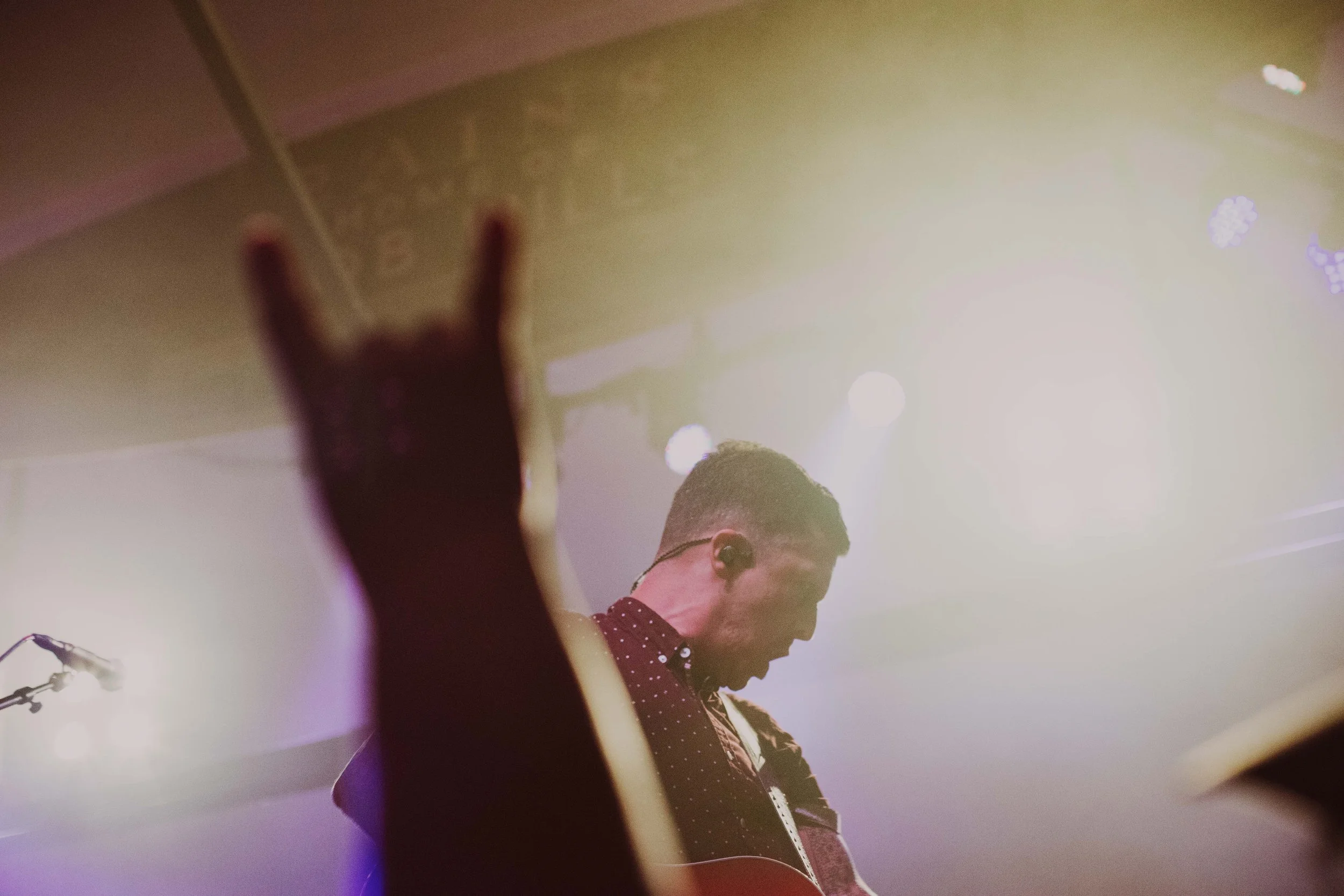 A musician playing guitar on stage, seen from below with stage lights in the background.