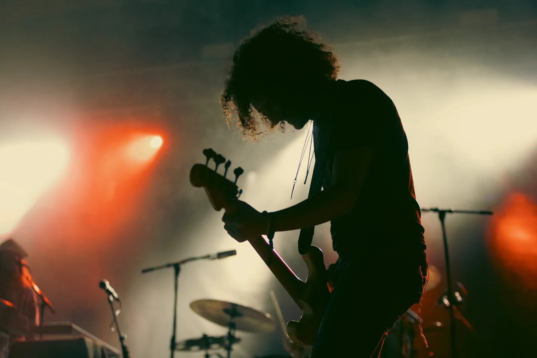 Silhouette of a musician playing an electric guitar on stage with stage lights illuminating in the background.