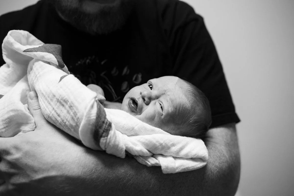 A newborn baby wrapped in a blanket being held by an adult
