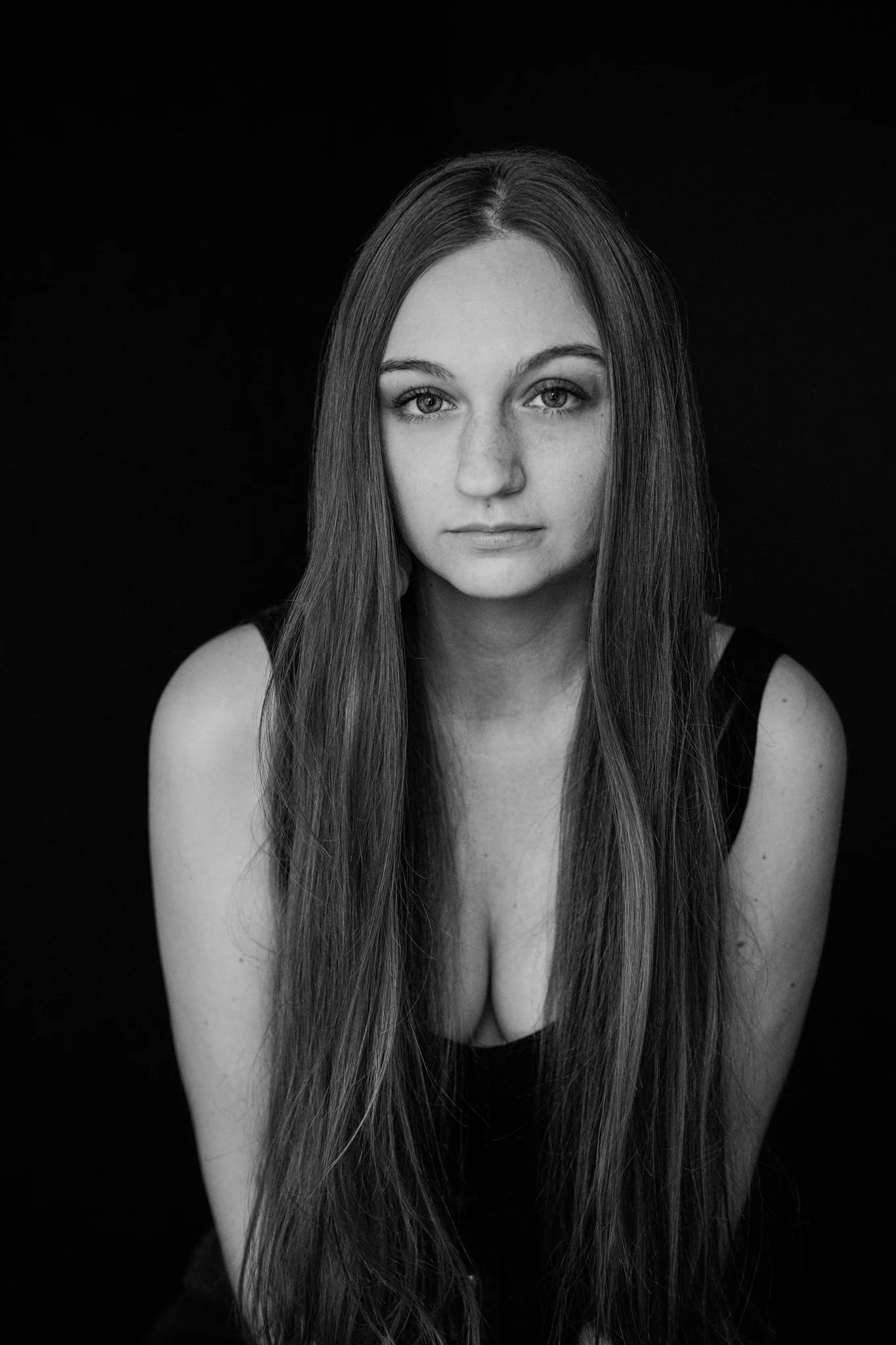 Black and white portrait of a young woman with long hair, looking directly at the camera against a dark background.