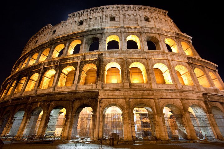 The illuminated exterior of the Colosseum at night, showing its stone arches and ancient architecture.