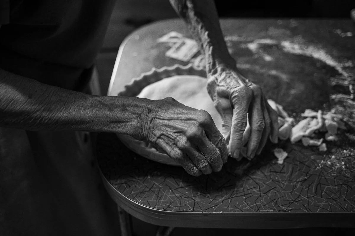 Close-up of elderly hands kneading dough on a dark patterned surface.