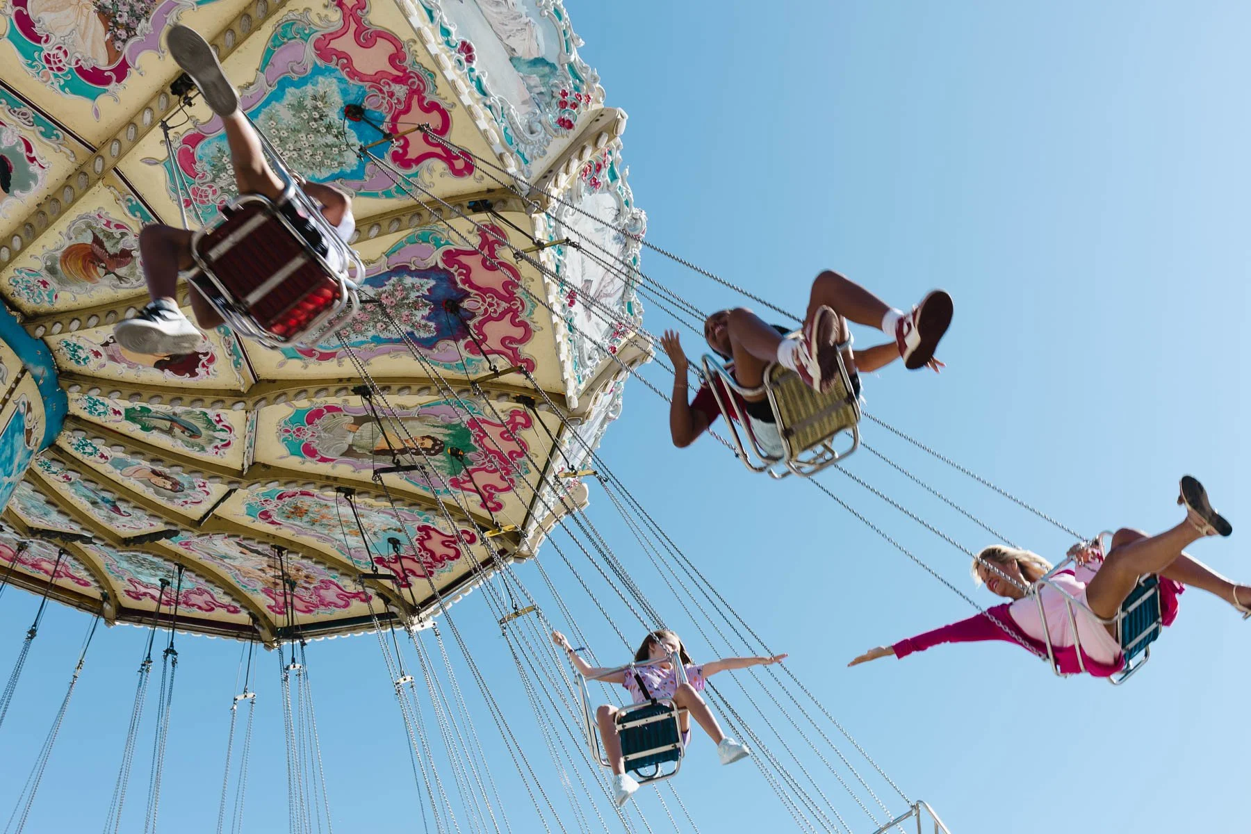 People on a colorful carousel swing ride at an amusement park, with a clear blue sky in the background.