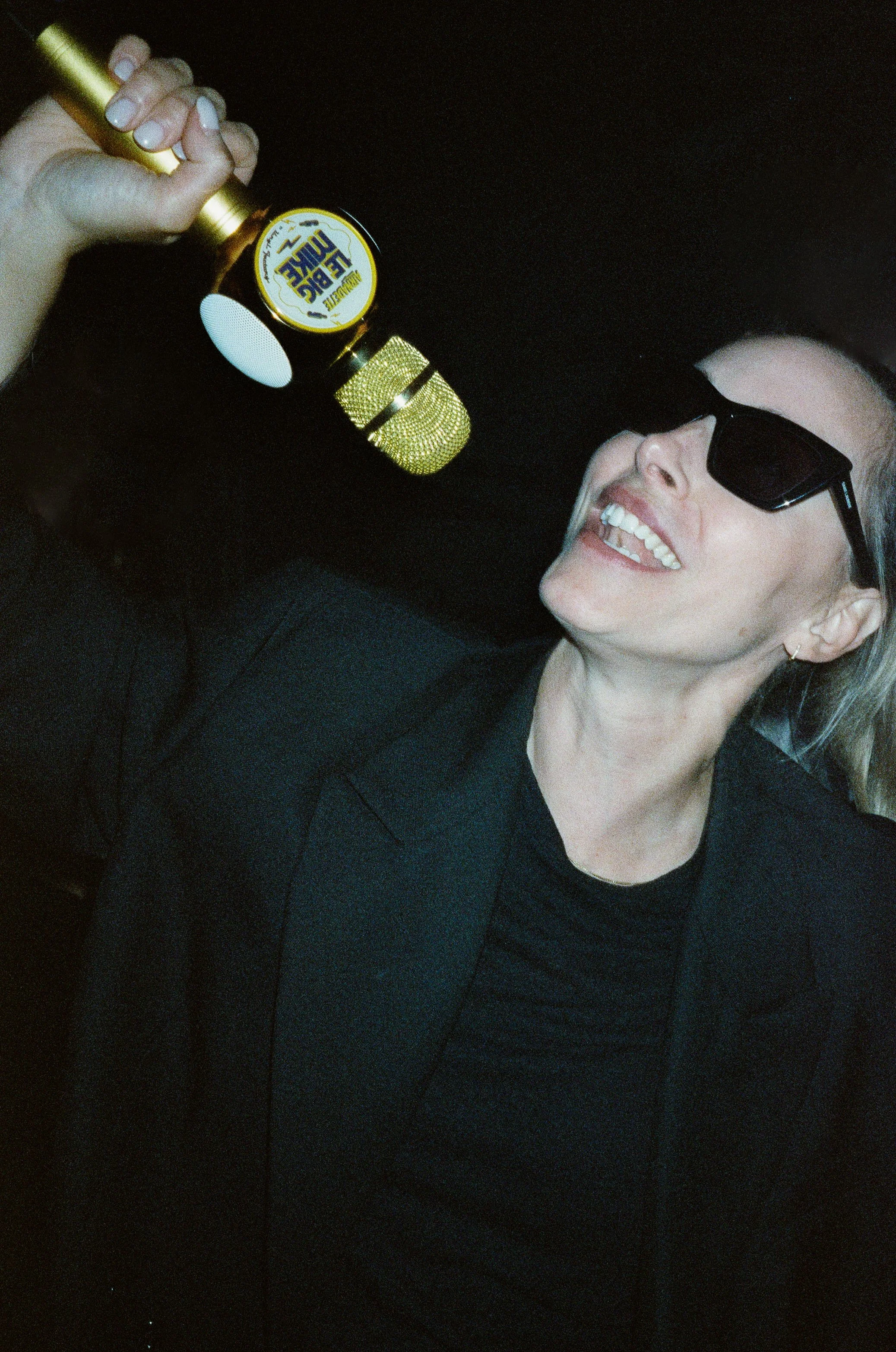 A woman in sunglasses smiling and holding a gold microphone labeled 'Blue Live'.