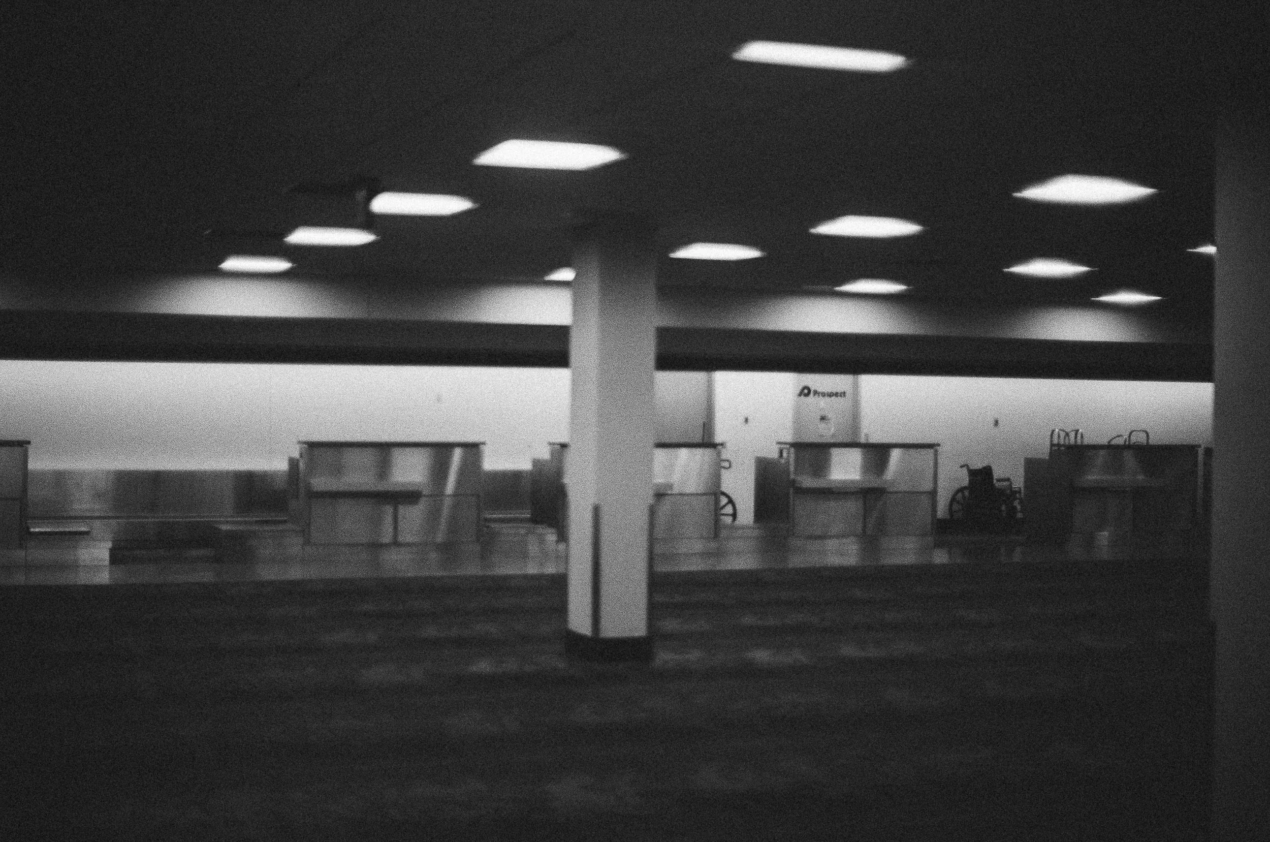Empty airport check-in counters and wheelchairs in a dimly lit terminal.