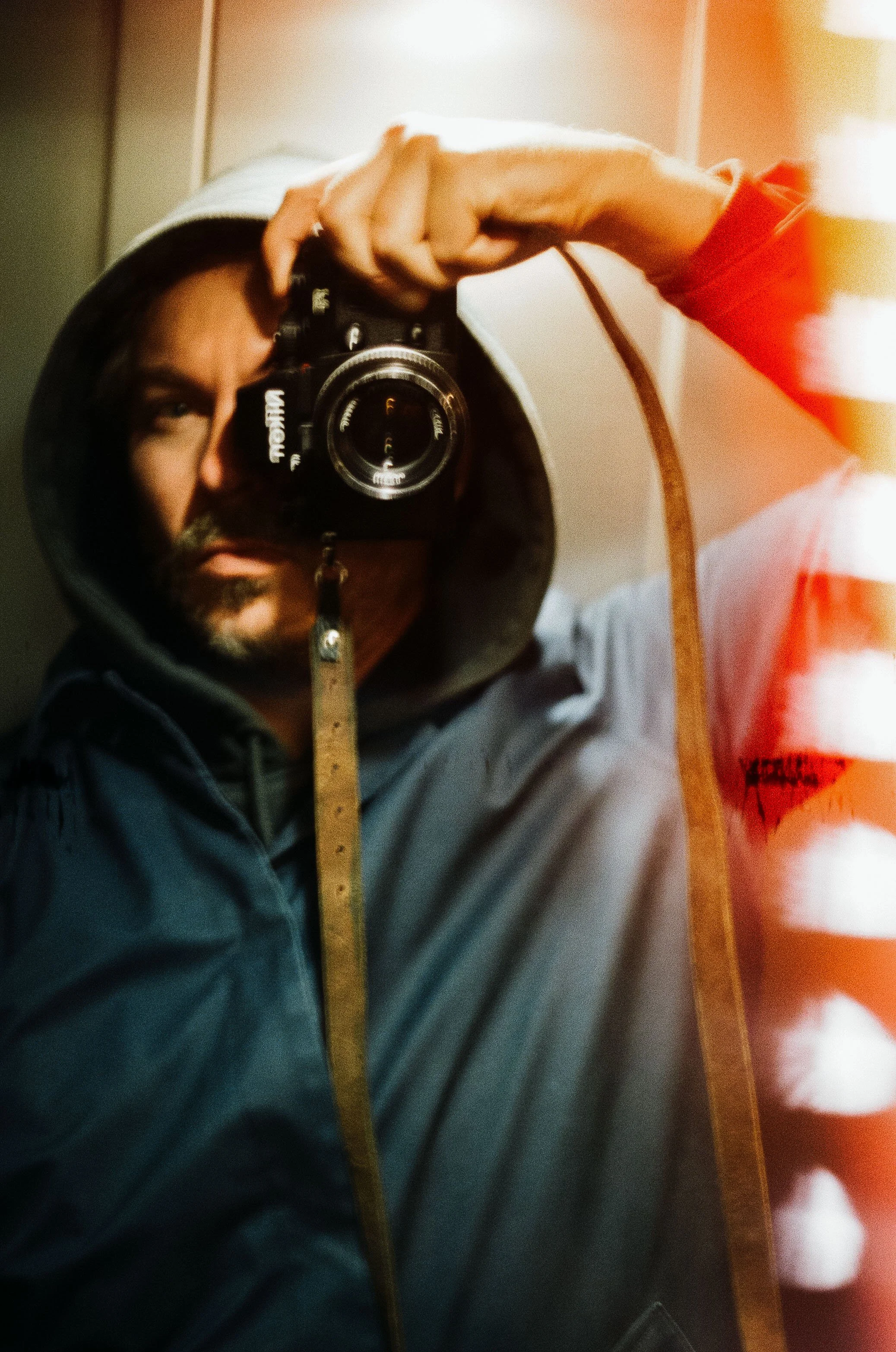 Man taking a mirror selfie with a camera, wearing a hooded sweatshirt, and holding a measuring tape.